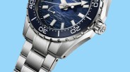 Close-up of a stainless steel dive watch with a blue textured dial, silver hour markers, and a rotating bezel.