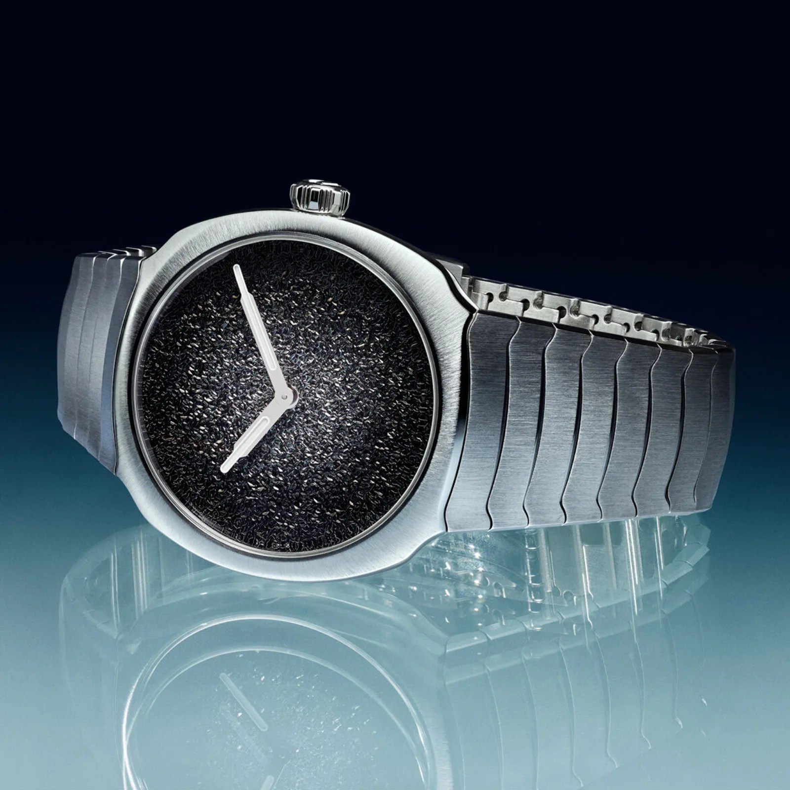 Silver metal wristwatch with a textured black dial and silver hands on a reflective surface.