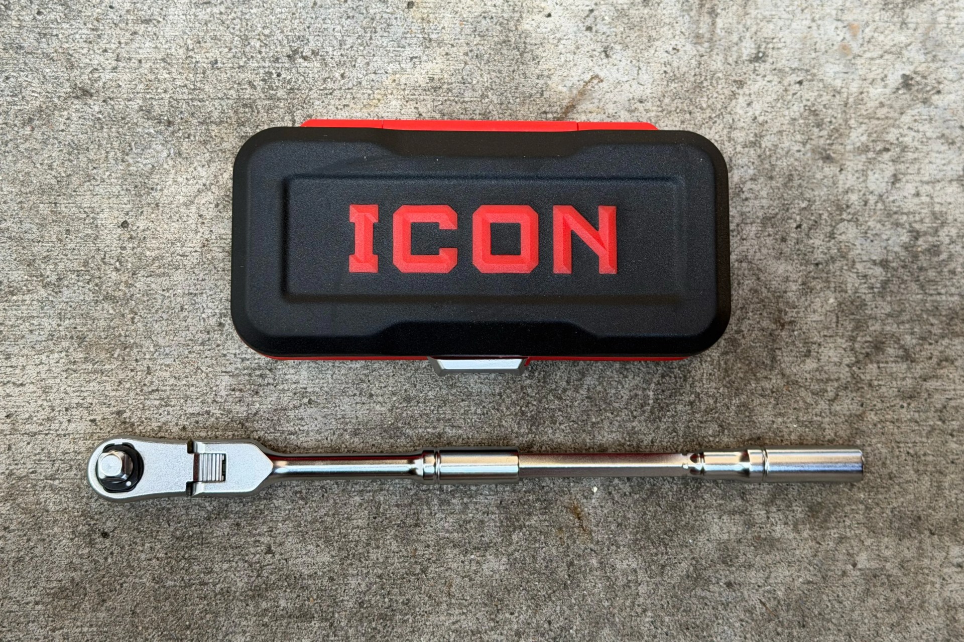 Black and red ICON branded toolbox with a silver ratchet wrench on a concrete surface.