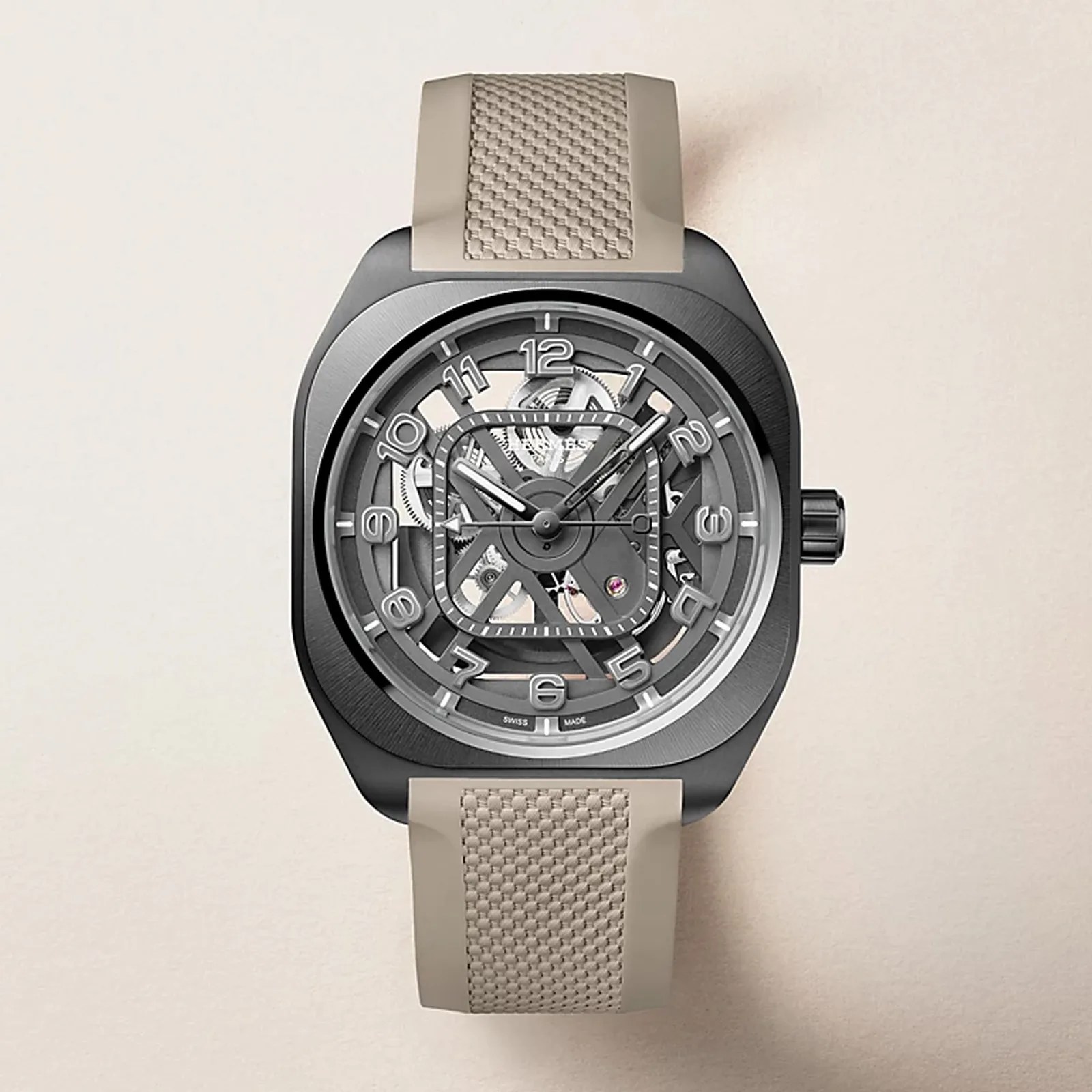 Square black watch with a skeleton dial and beige textured rubber strap.