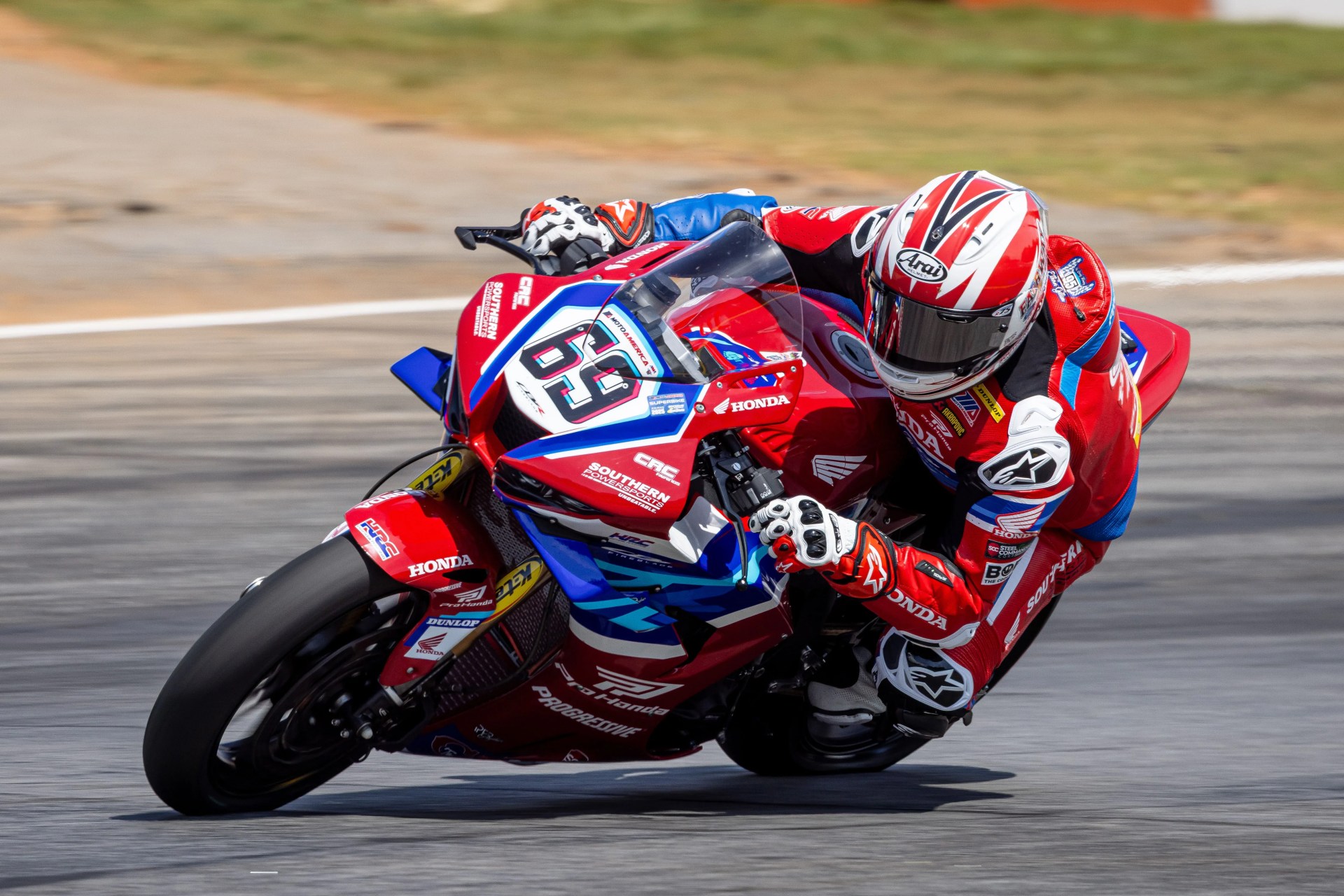 Motorcycle racer in red, blue, and white gear leaning into a turn on a red Honda racing bike numbered 69.