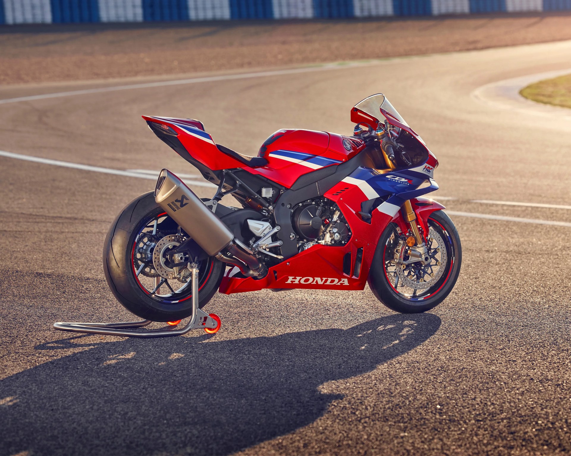 Red, blue, and white Honda sport motorcycle on a race track with a rear stand.