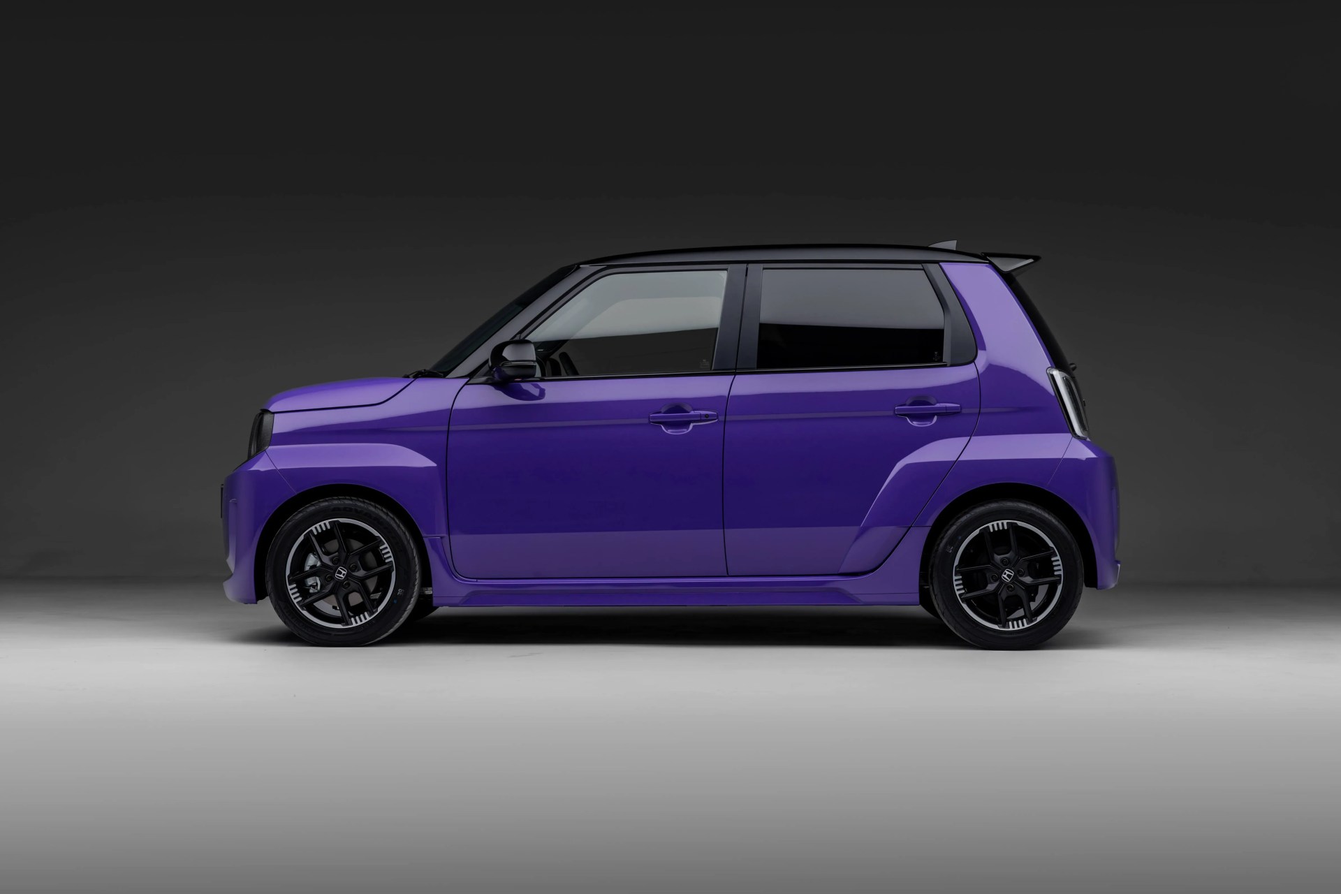 Compact purple hatchback car with black roof and sporty black alloy wheels on a gray studio floor.