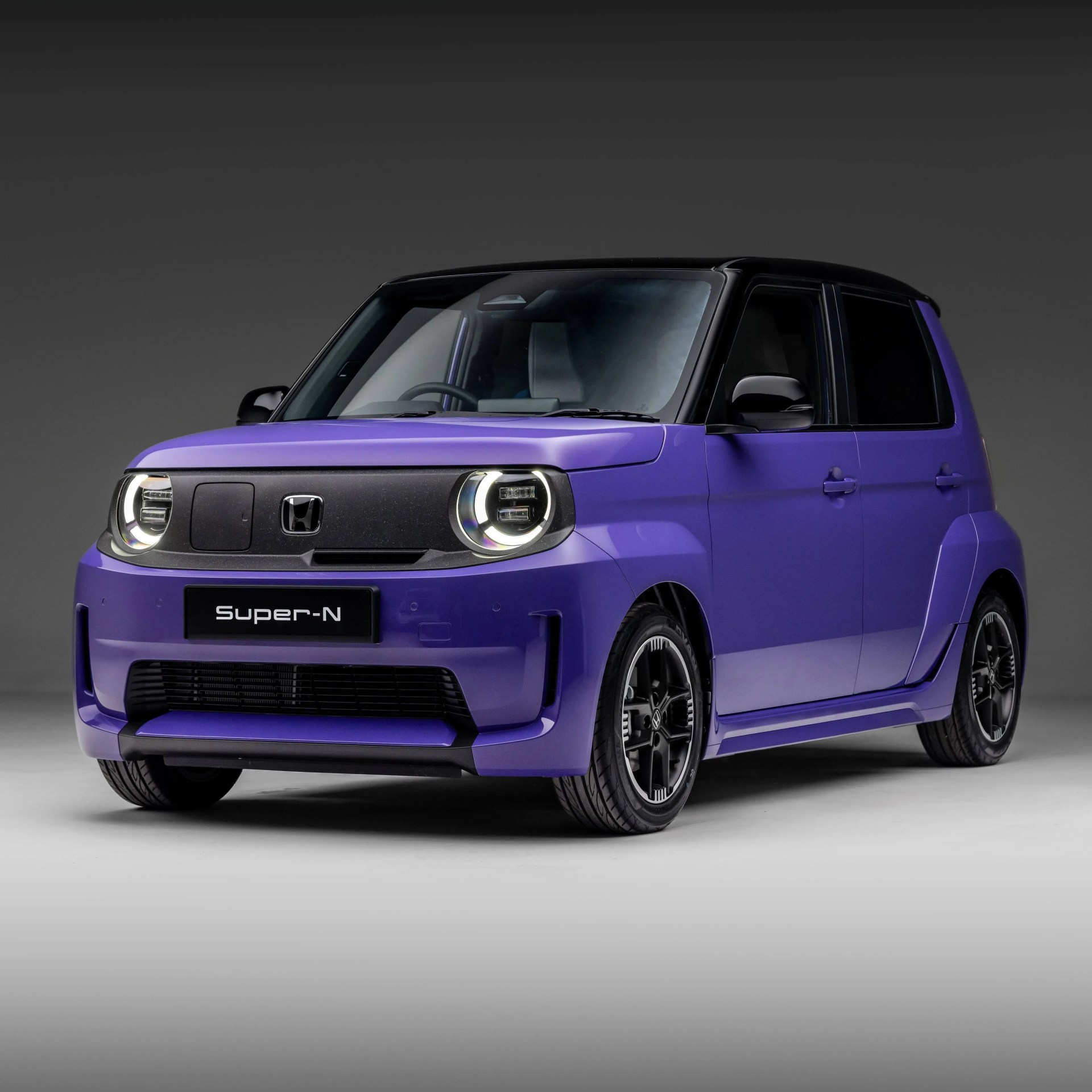 Compact purple Honda Super-N car with black roof and round LED headlights on a gray studio floor.