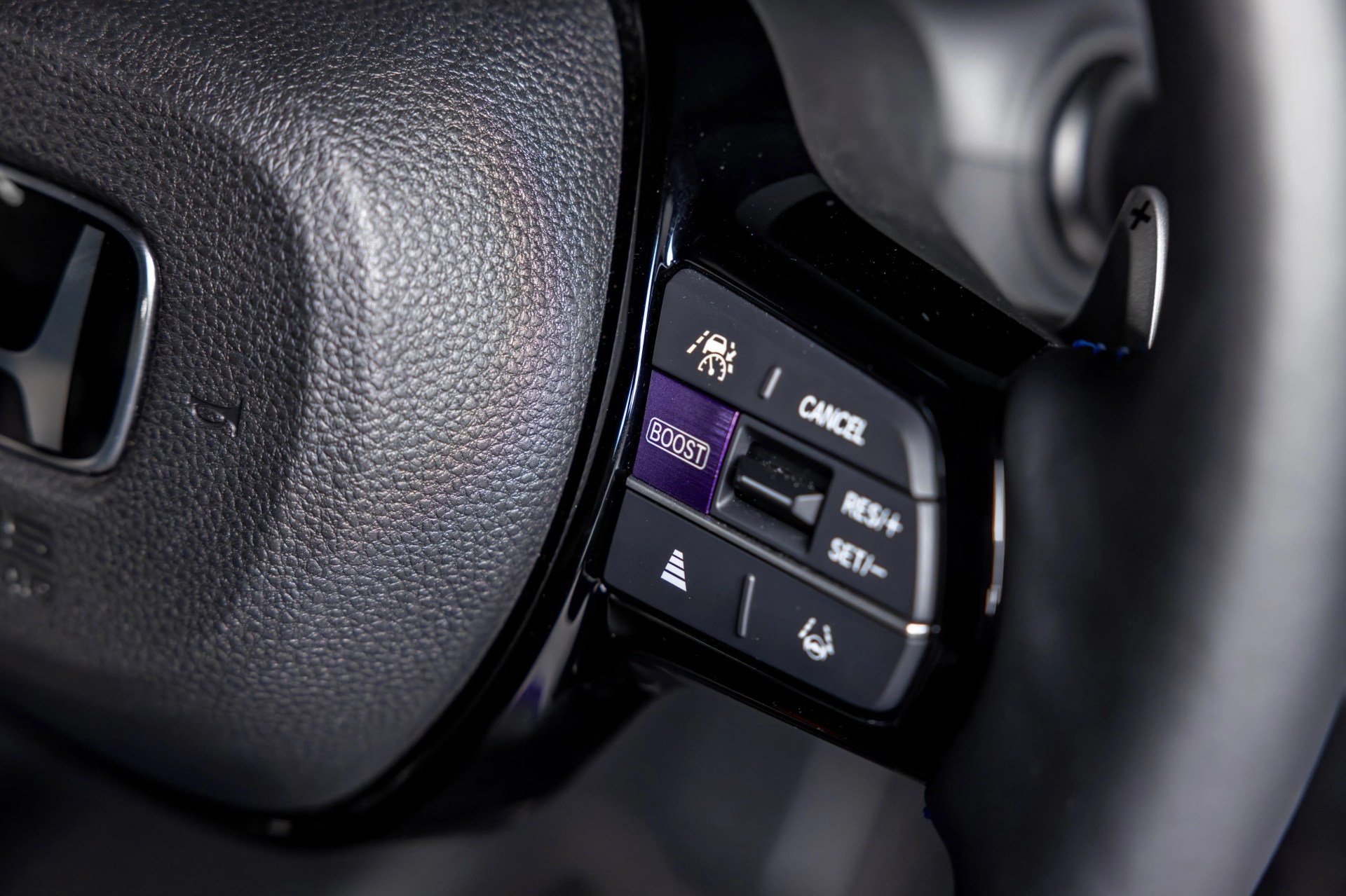 Close-up of a car steering wheel with cruise control buttons, including a purple "BOOST" button and paddle shifter.