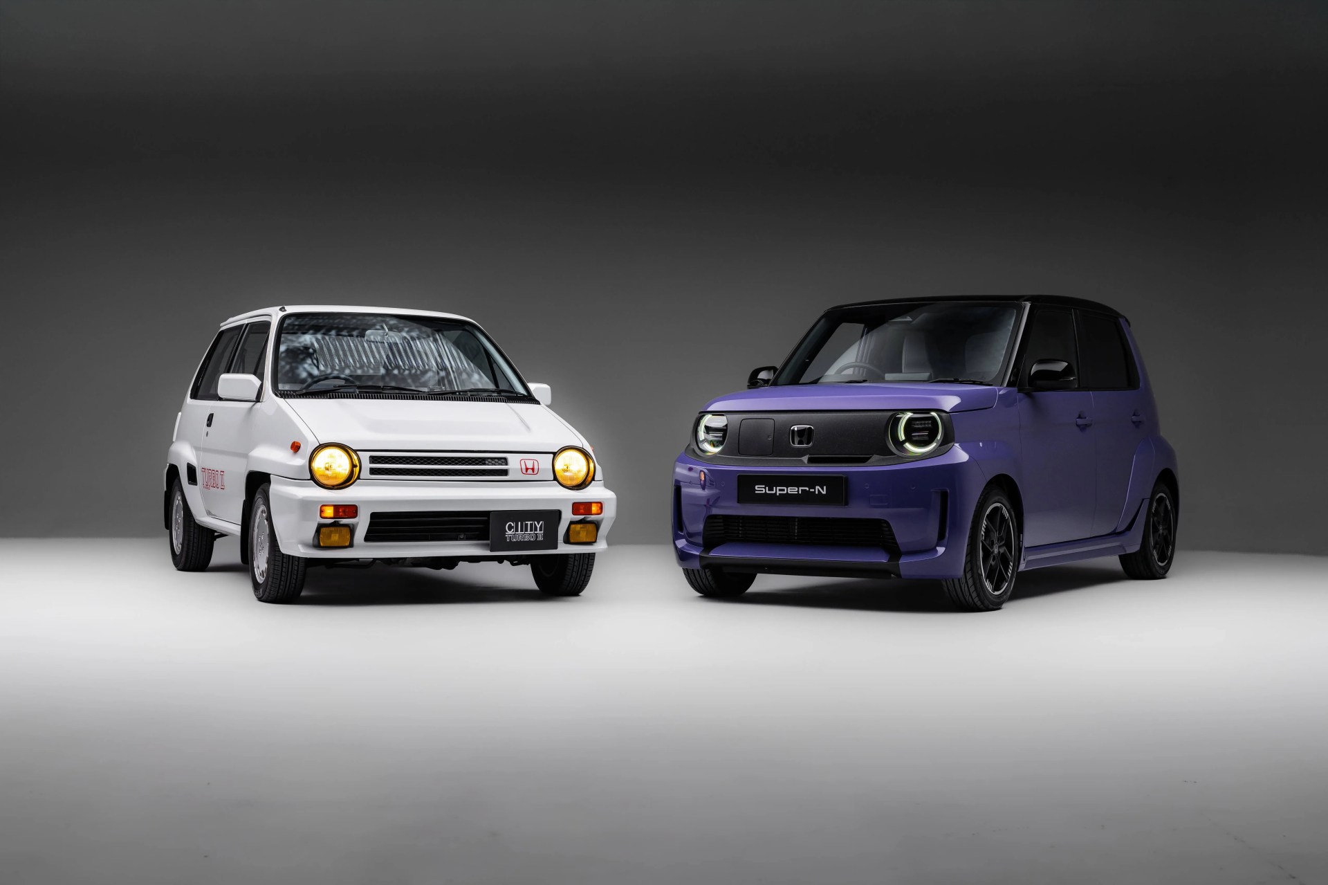 Two compact Honda cars, a white vintage model with yellow headlights and a purple modern model with circular LED headlights, side by side in a studio.