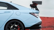 Light blue sports car rear side with black alloy wheel, red brake caliper, and large carbon fiber rear wing.