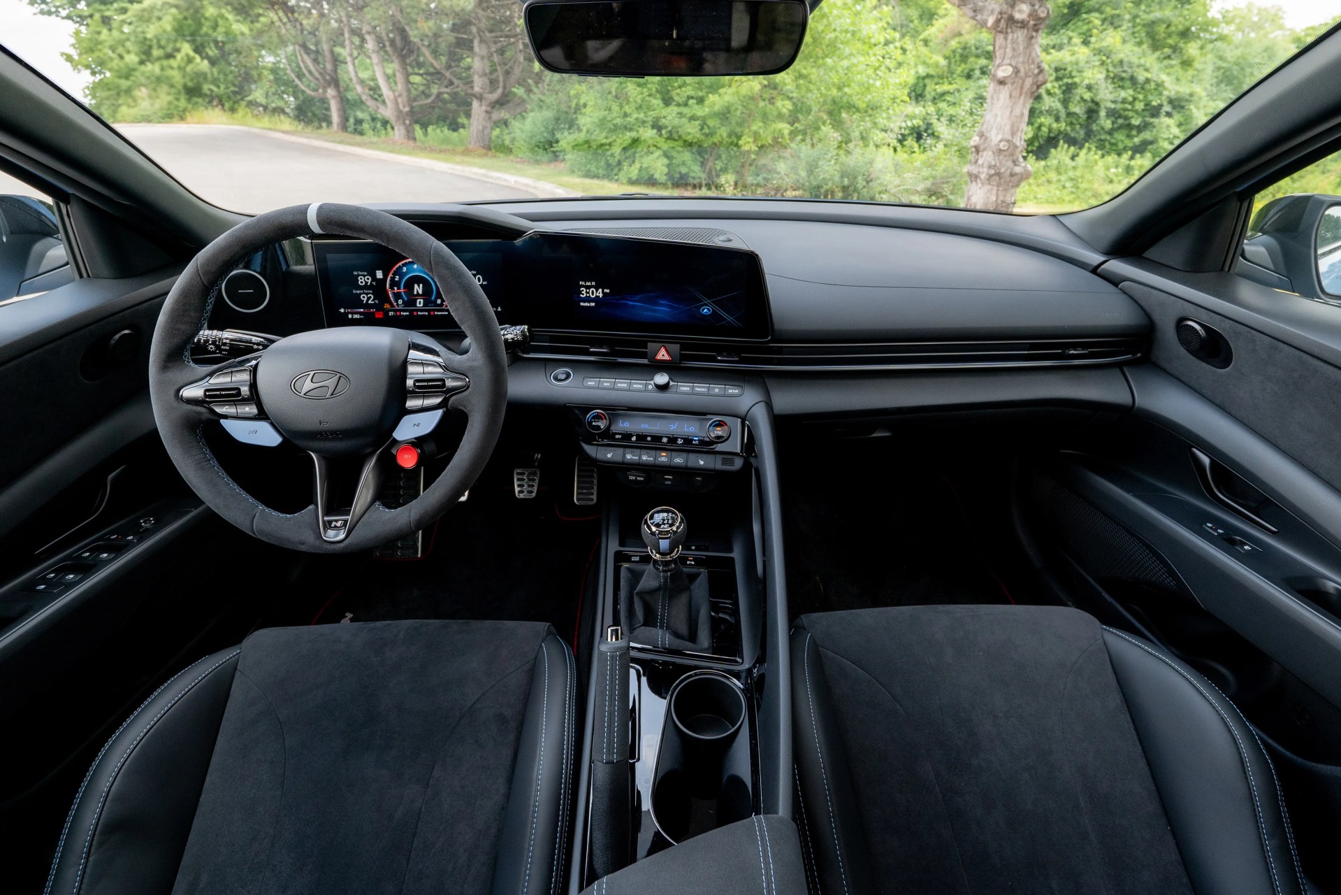Interior of a Hyundai car with a black suede steering wheel, digital dashboard, manual gear shift, and black seats.