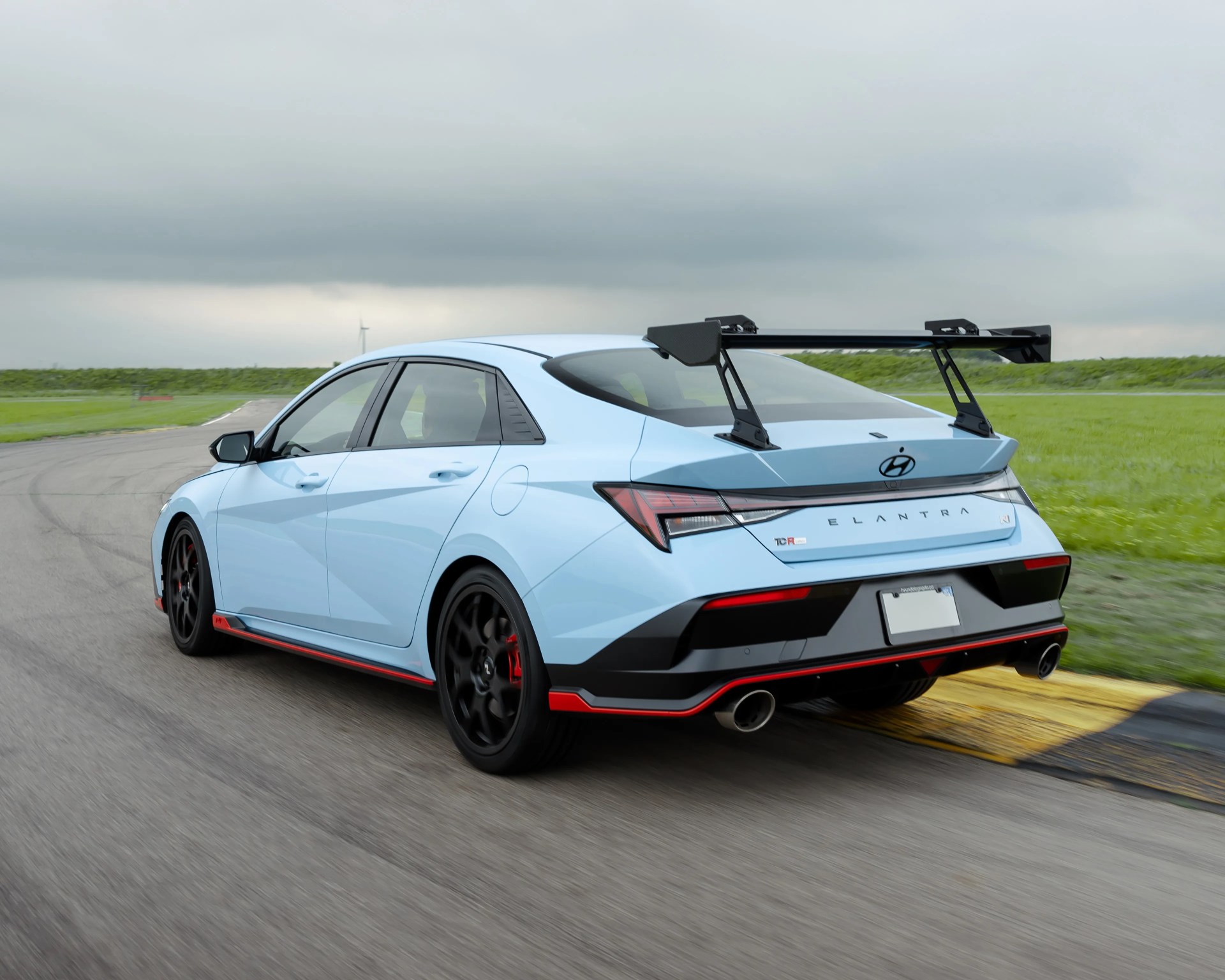 Light blue Hyundai Elantra N sedan with black and red accents and a large rear spoiler on a racetrack.