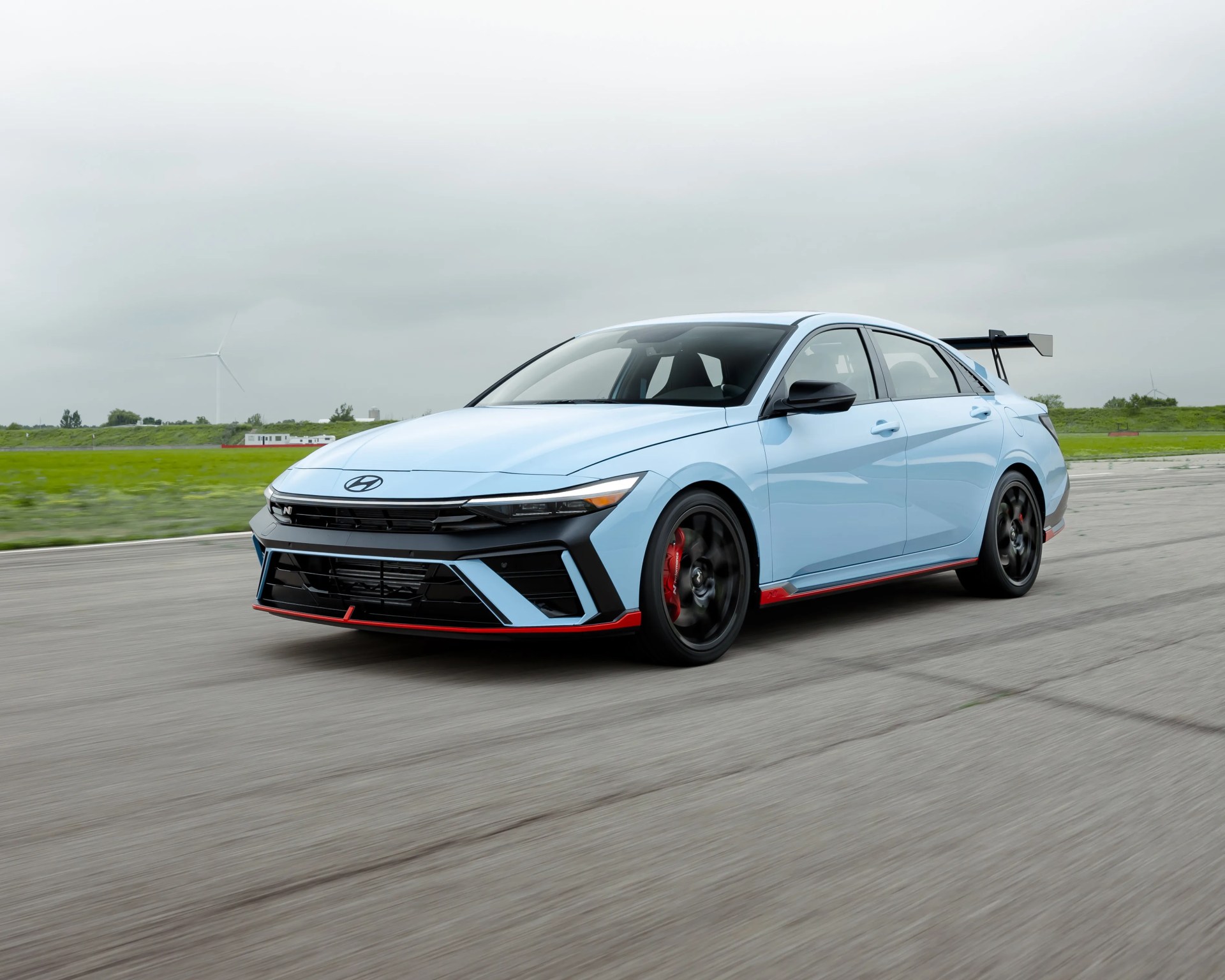 Light blue Hyundai sedan with black and red accents and a large rear spoiler driving on a paved road.