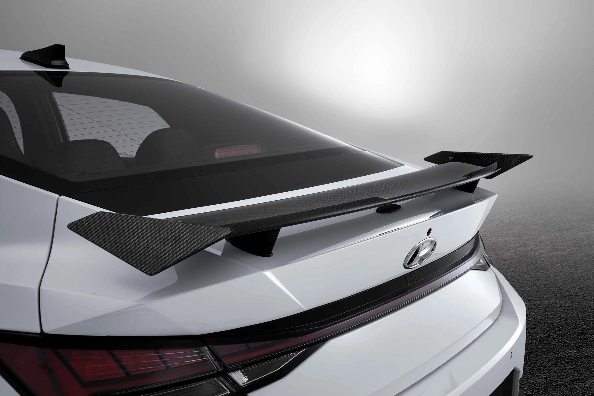 Rear view of a white Hyundai car with a black carbon fiber spoiler attached to the trunk.