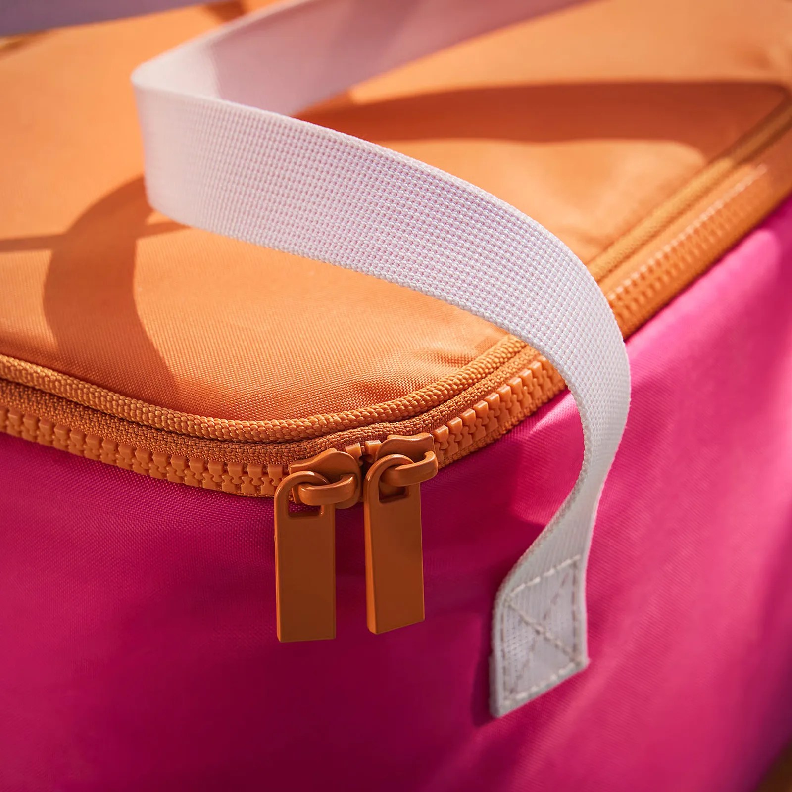 Close-up of orange zipper and white strap on pink and orange fabric bag.