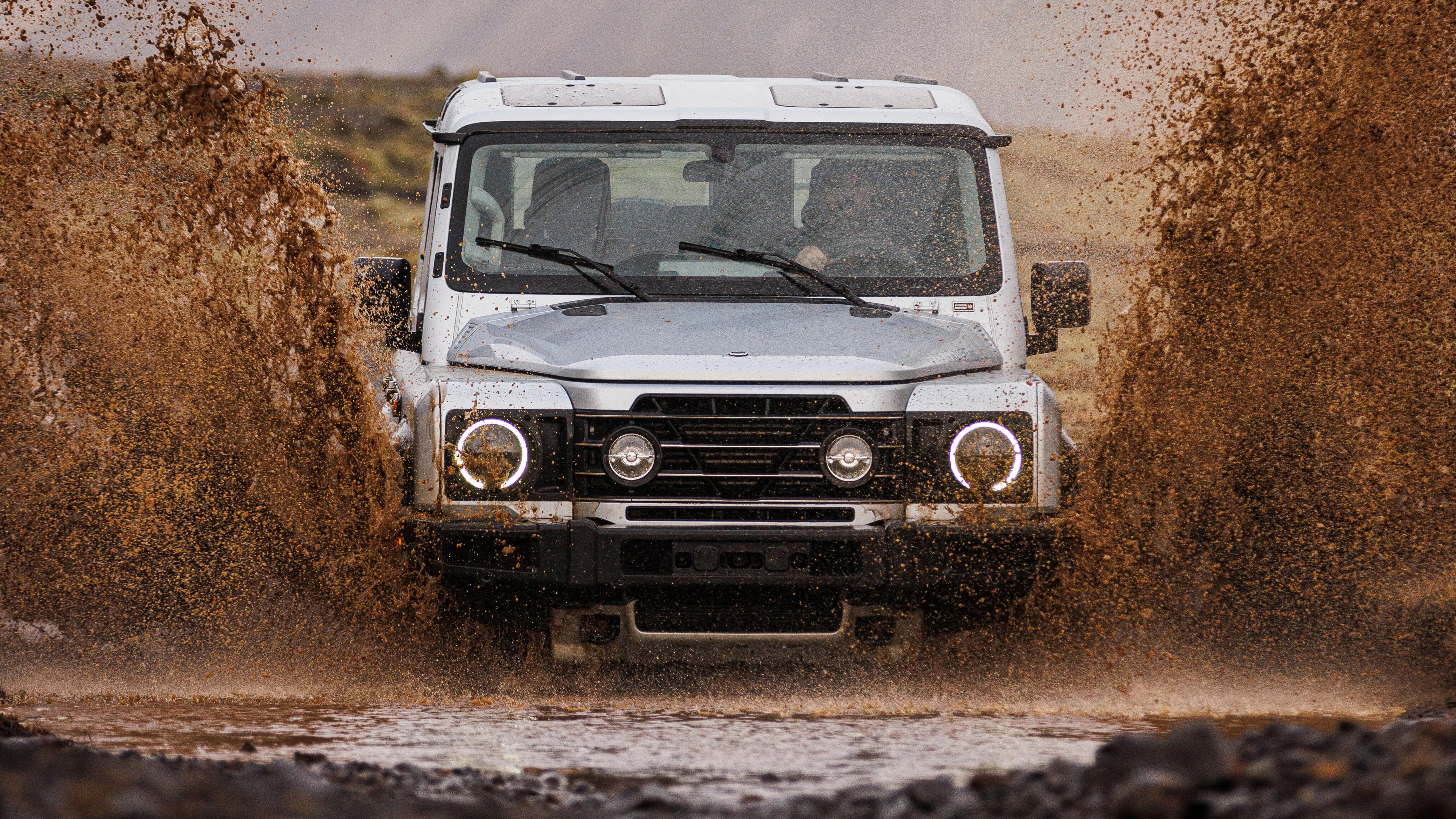 White off-road SUV splashing muddy water while driving through a shallow puddle.