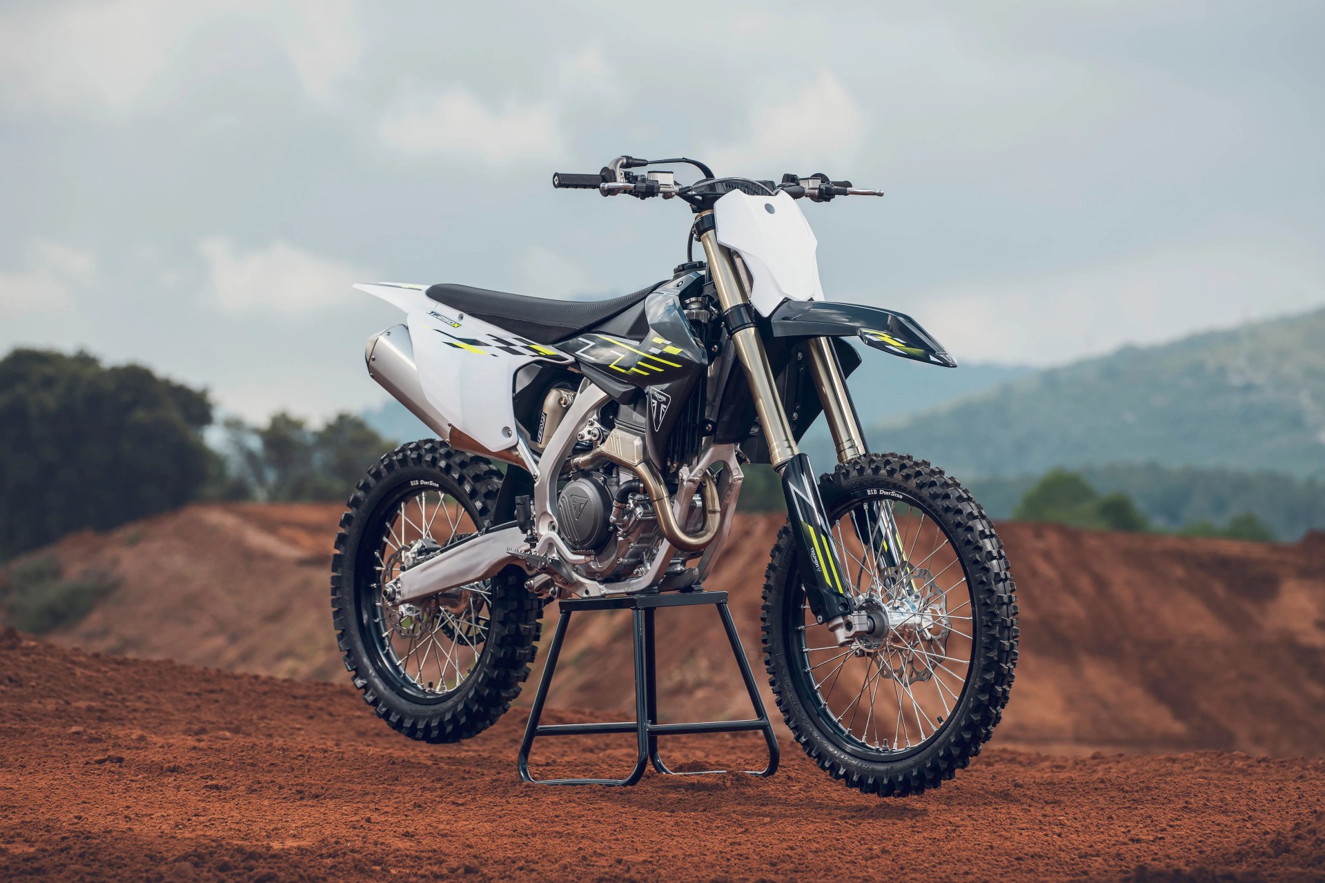 Black and white dirt bike with yellow accents on a black stand on red dirt track.