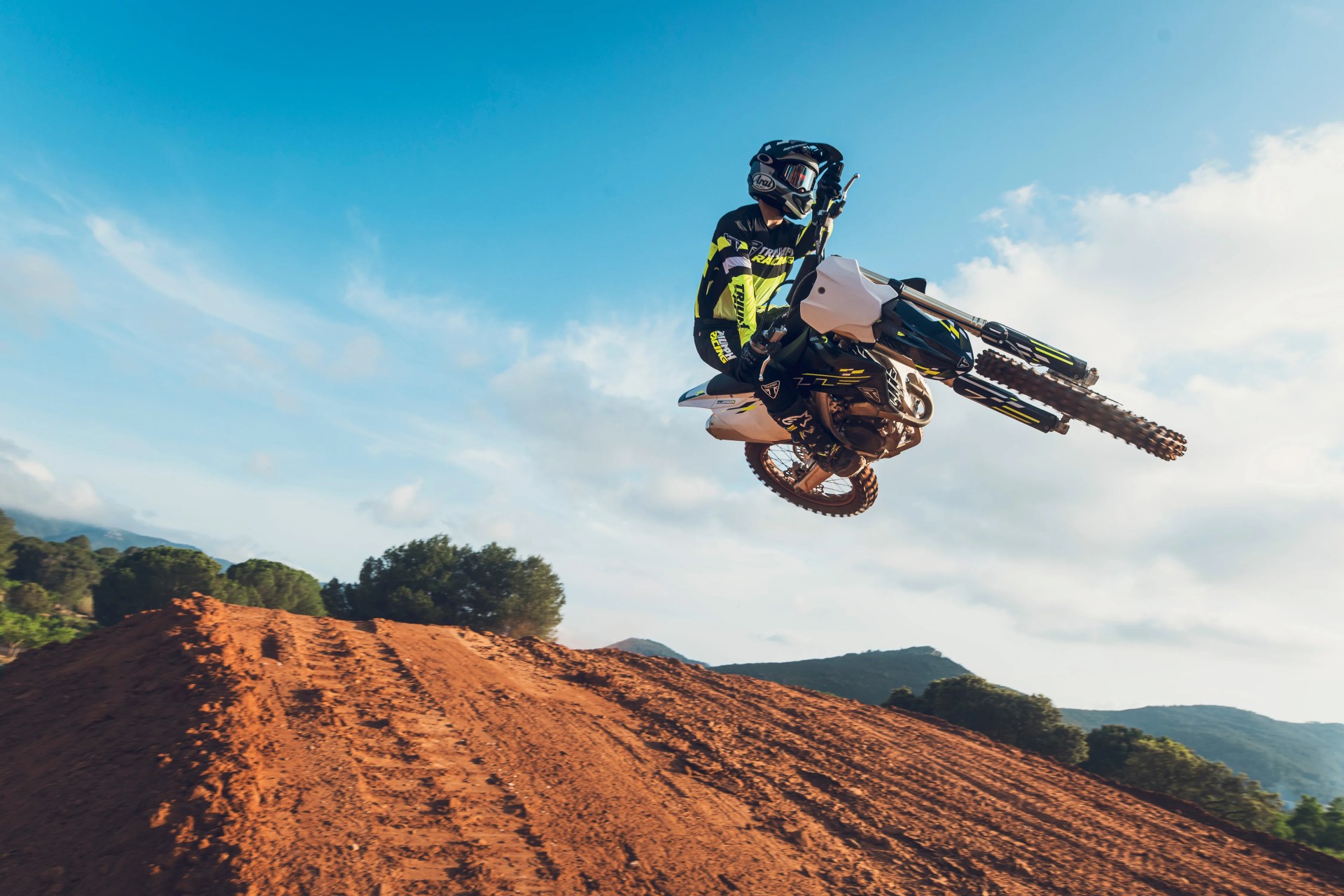 Motocross rider in black and yellow gear performing a jump on a dirt track under a blue sky.