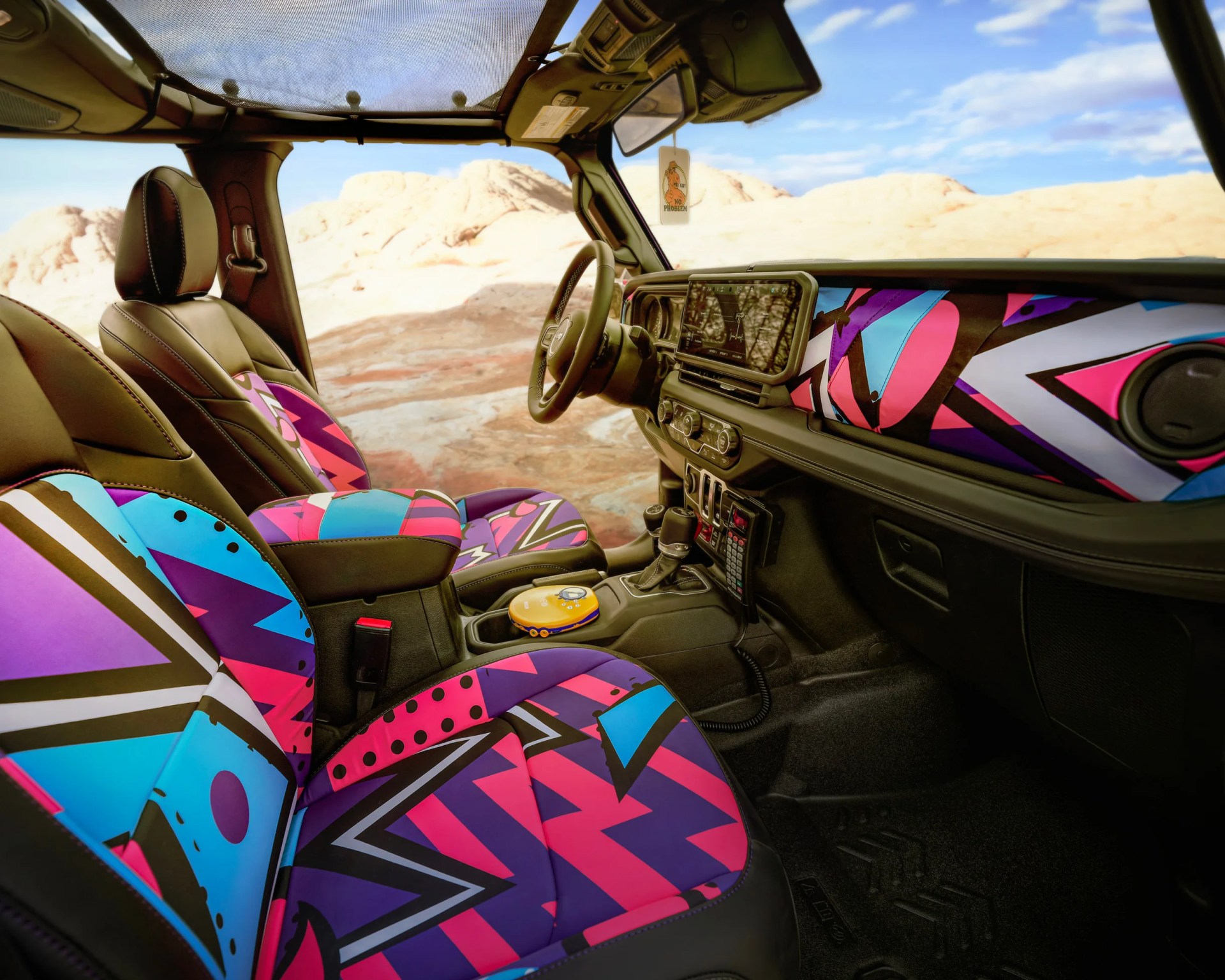 Car interior with black leather seats featuring vibrant geometric patterns in pink, blue, and purple, and matching dashboard accents.