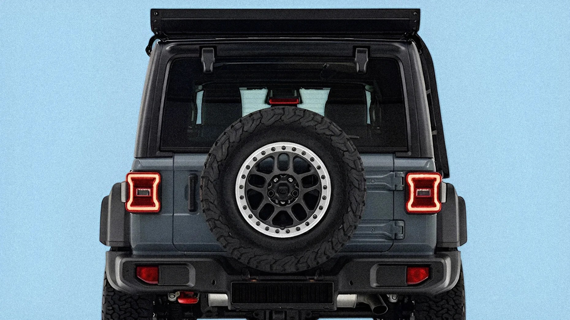 Rear view of a gray off-road SUV with a spare tire mounted on the back and illuminated taillights.
