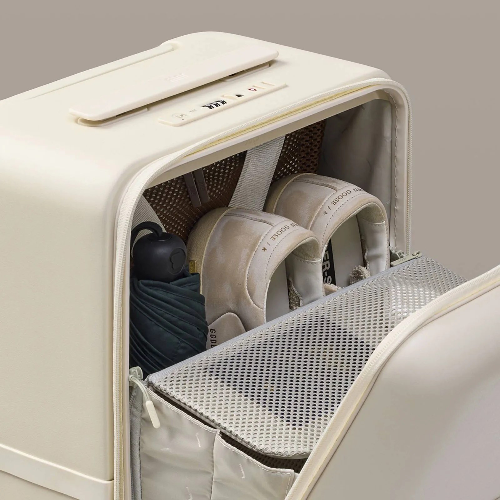 Beige hard-shell suitcase with a zippered compartment holding beige sneakers and a folded black umbrella.