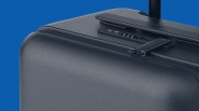 Close-up of a black hard-shell suitcase corner with a zipper and built-in combination lock against a blue background.