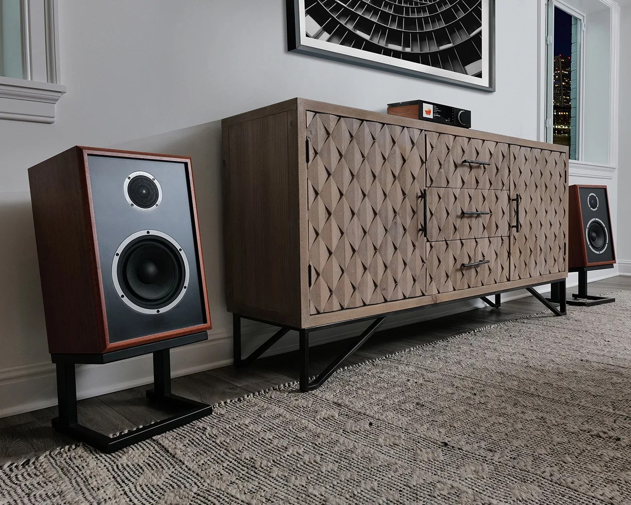 Pair of vintage-style wooden speakers on black metal stands flanking a textured wooden sideboard with black metal legs in a modern room.