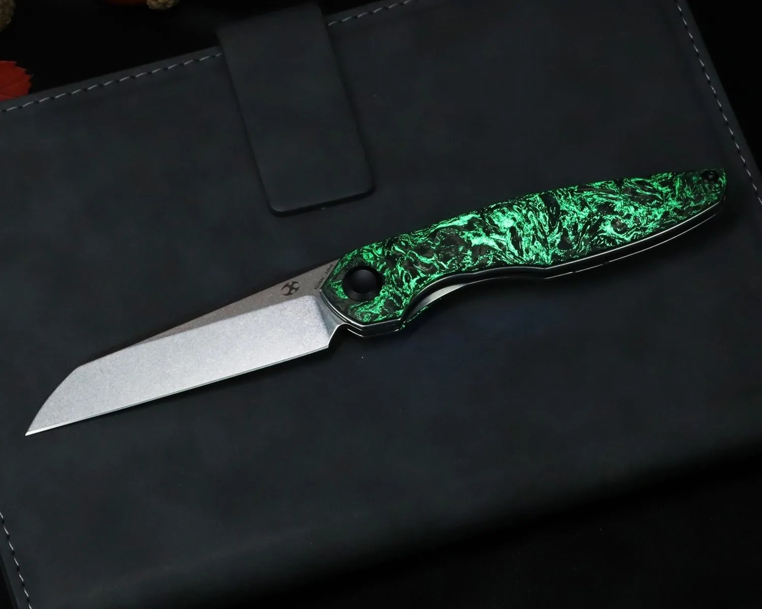 Folding knife with a stonewashed blade and a green marbled handle resting on a black leather surface.