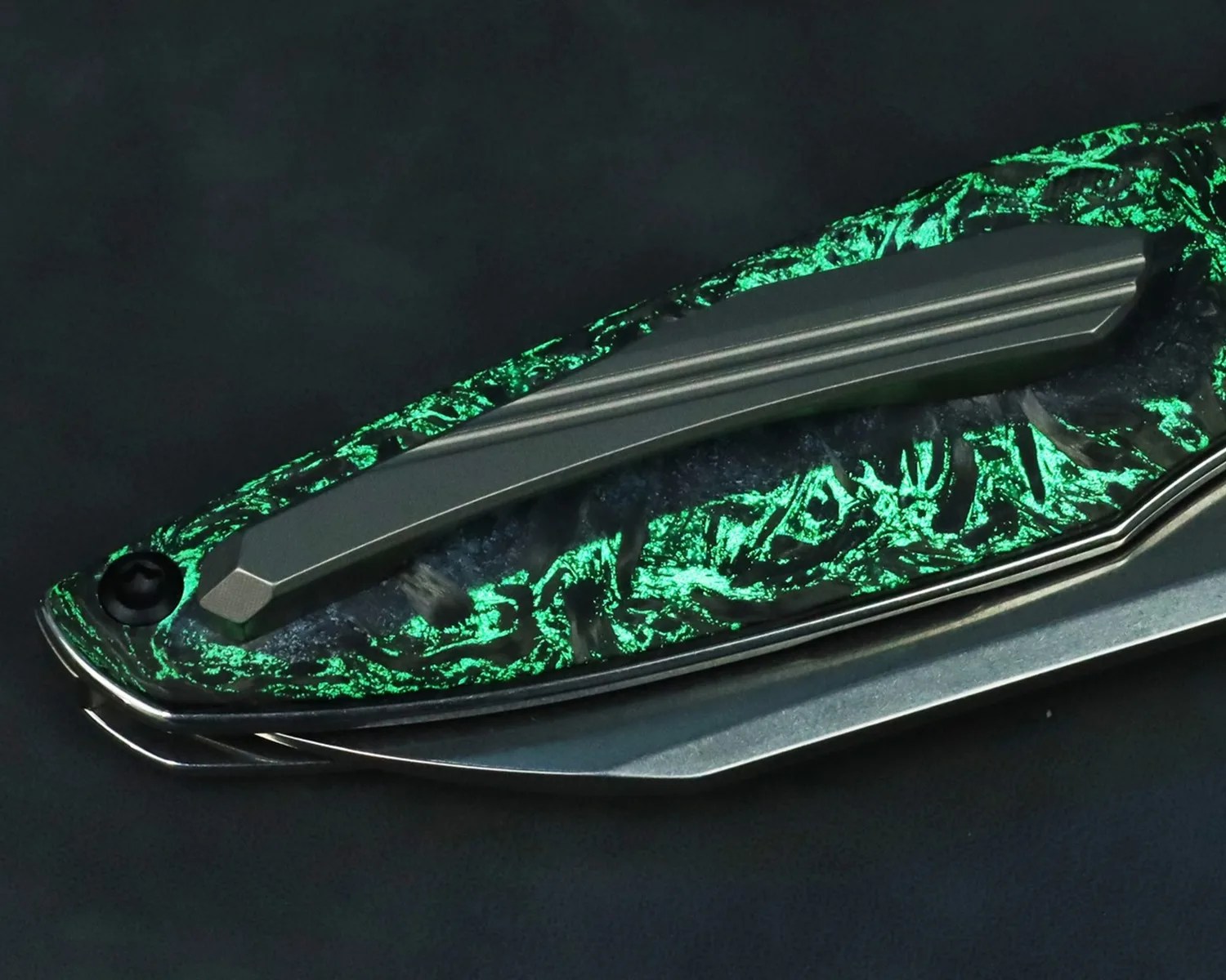 Close-up of a folding knife handle with a glowing green textured pattern and a matte metal clip.