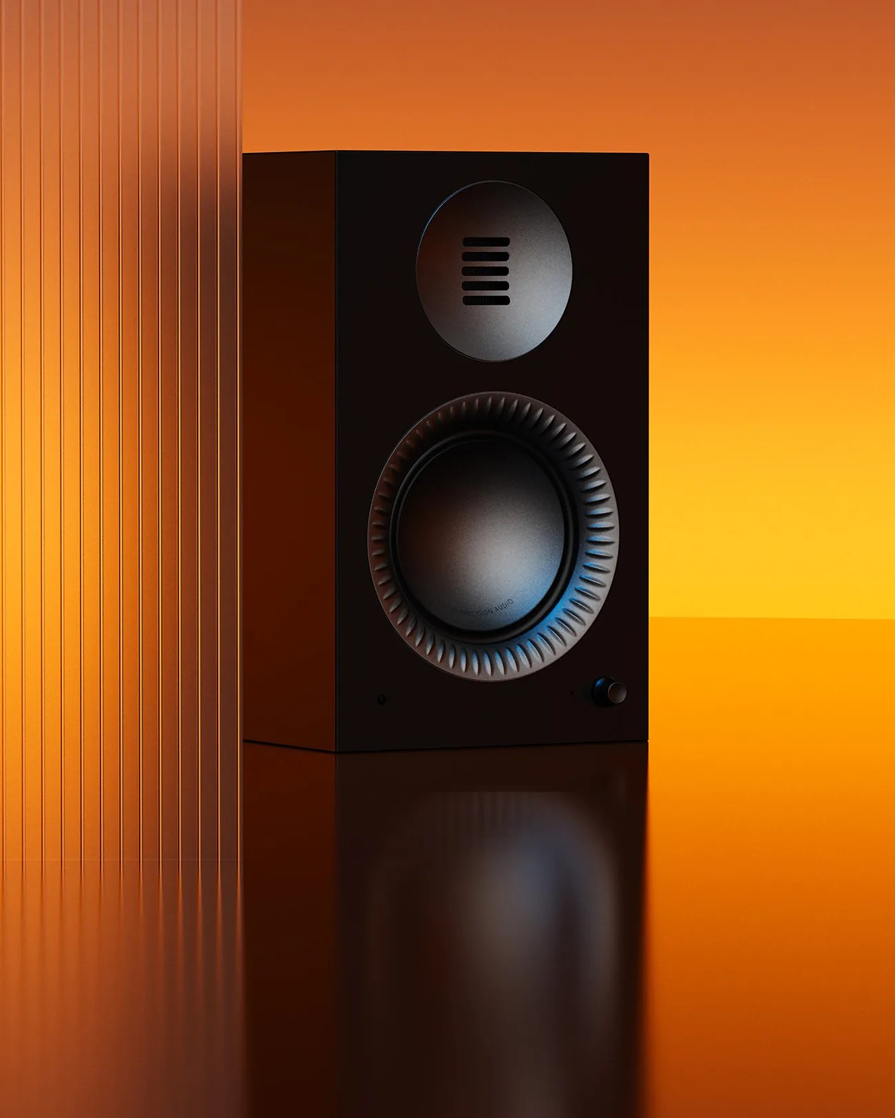 Black rectangular speaker with circular drivers and a small knob on an orange reflective surface.