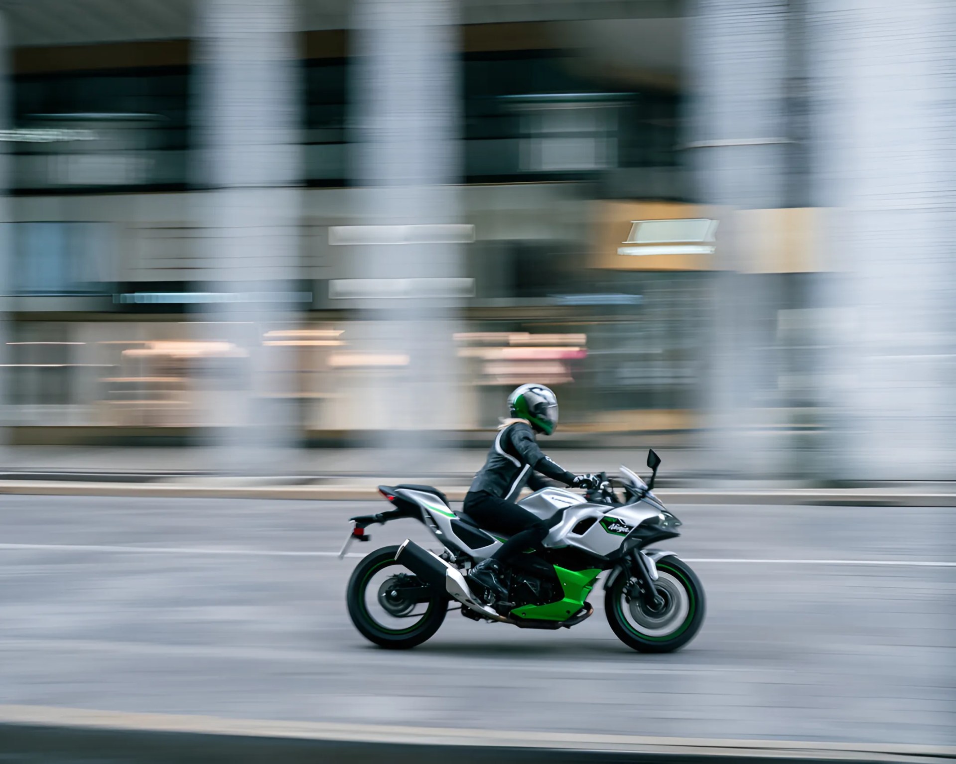 Person wearing black riding gear and green helmet riding a silver and green sport motorcycle on a city street.