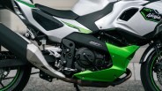 Close-up of a white and green Kawasaki Ninja HEV hybrid motorcycle engine and exhaust system.