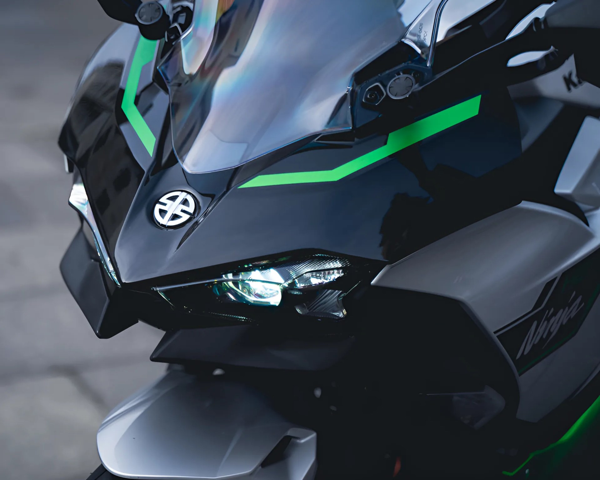 Close-up of a black and green Kawasaki Ninja motorcycle front with illuminated headlight and clear windshield.
