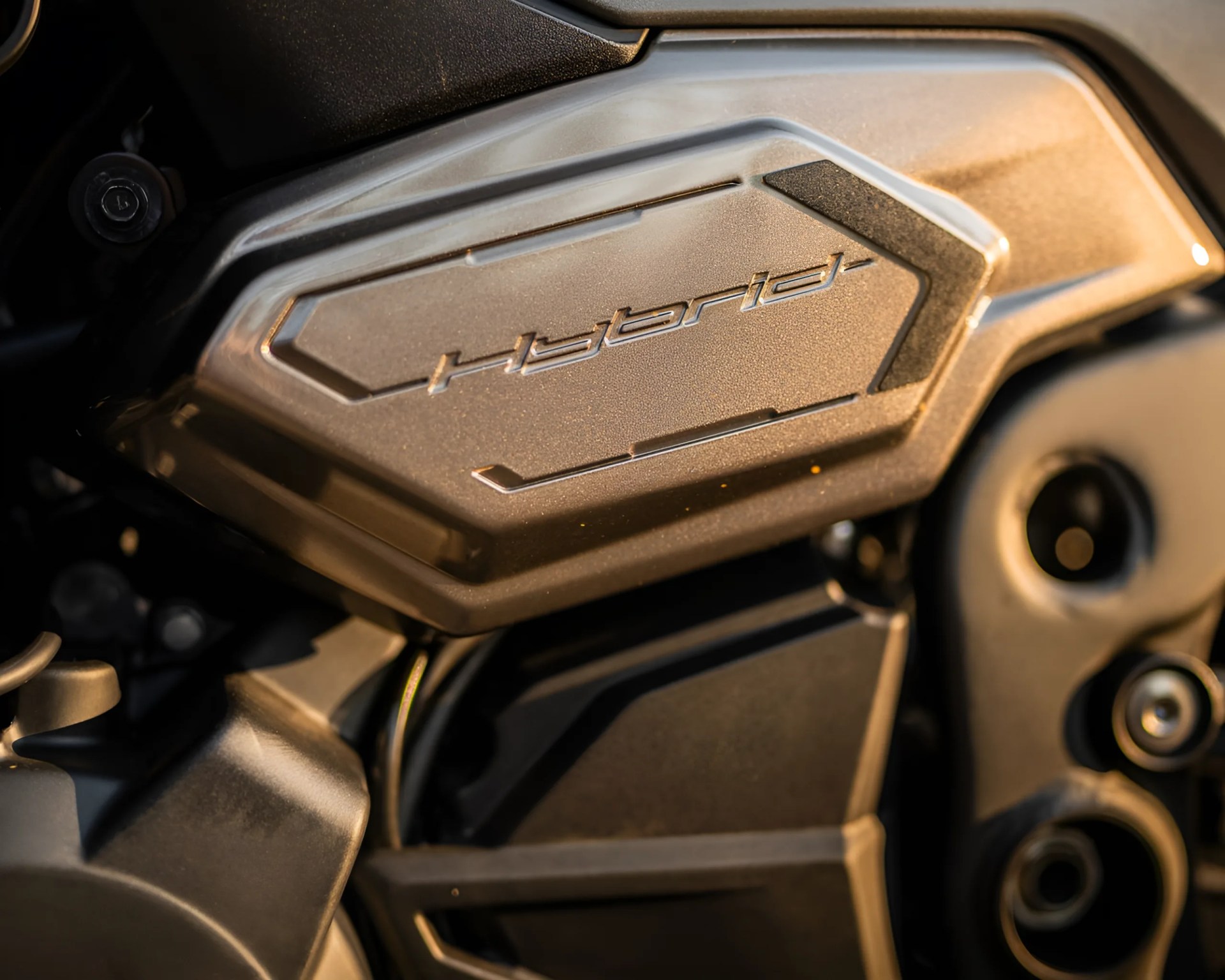 Close-up of a metallic motorcycle engine cover with the word "Hybrid" embossed on it.