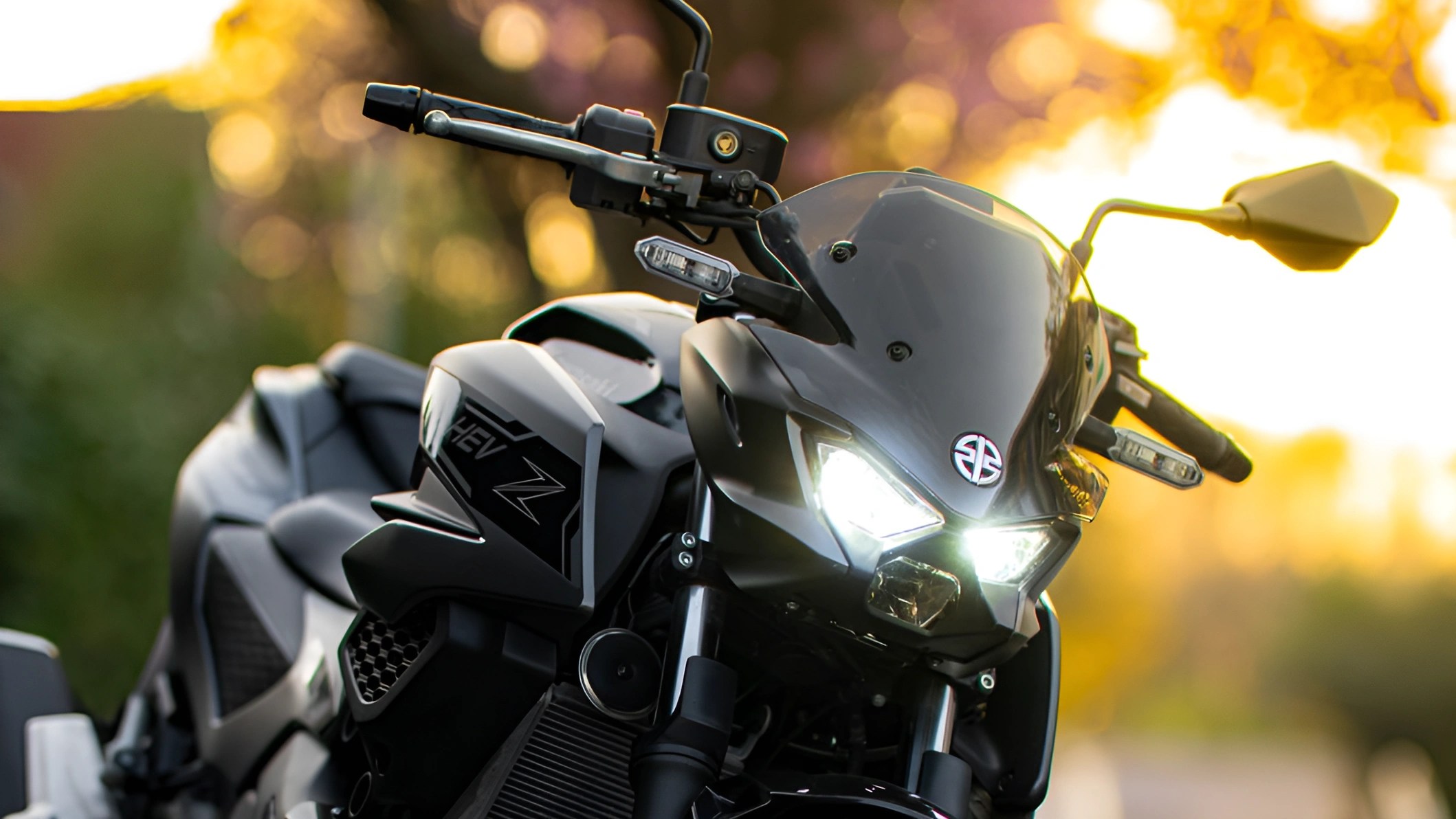 Black sport motorcycle with illuminated headlights and "HEV Z" decal on side panel at sunset.