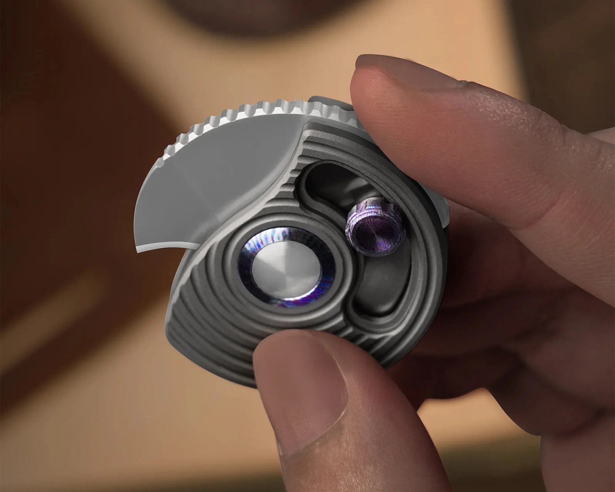 Hand holding a small, round, metallic mechanical component with two visible lenses or sensors.