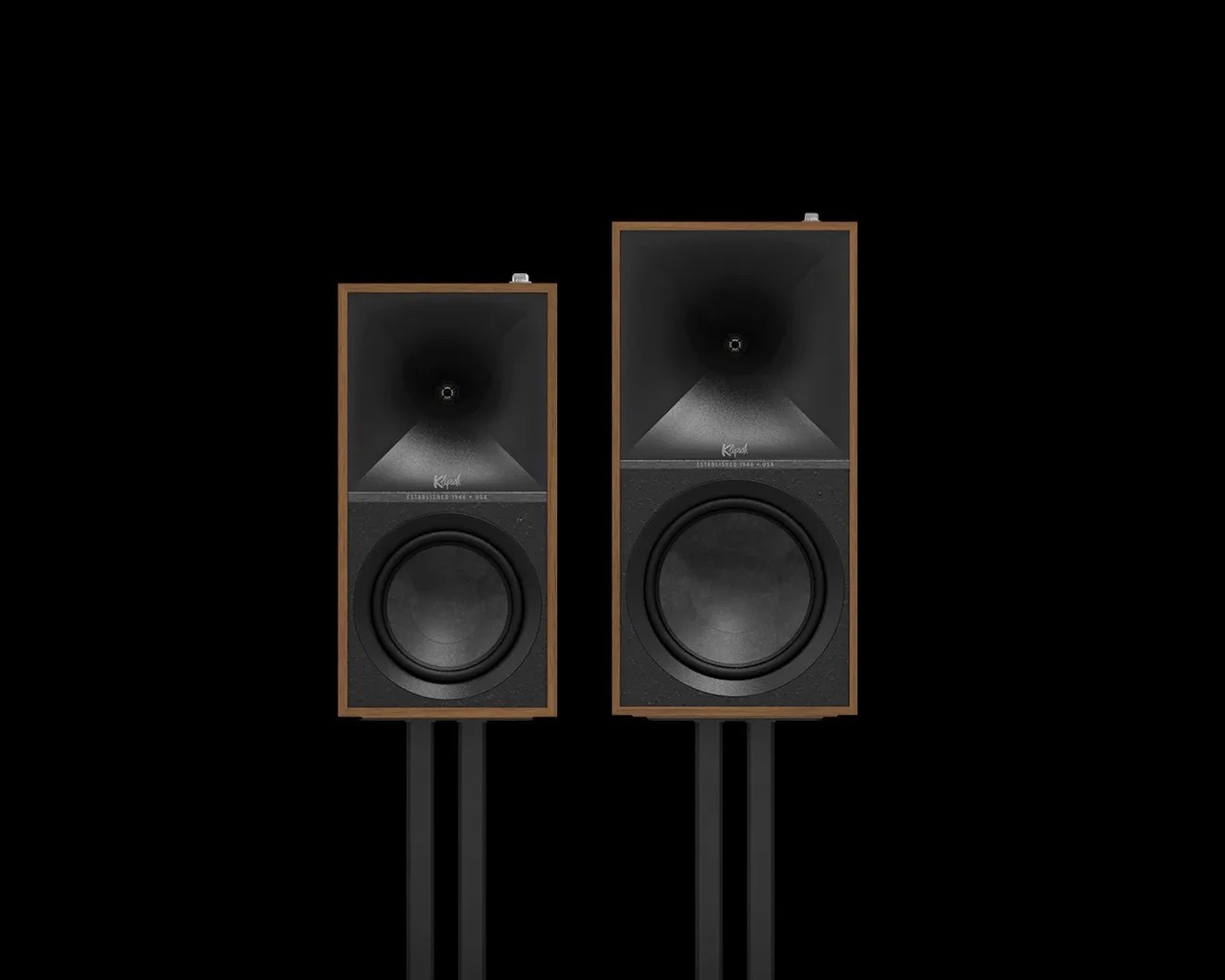Pair of Klipsch speakers with wooden frames and black front panels, mounted on black stands against a black background.