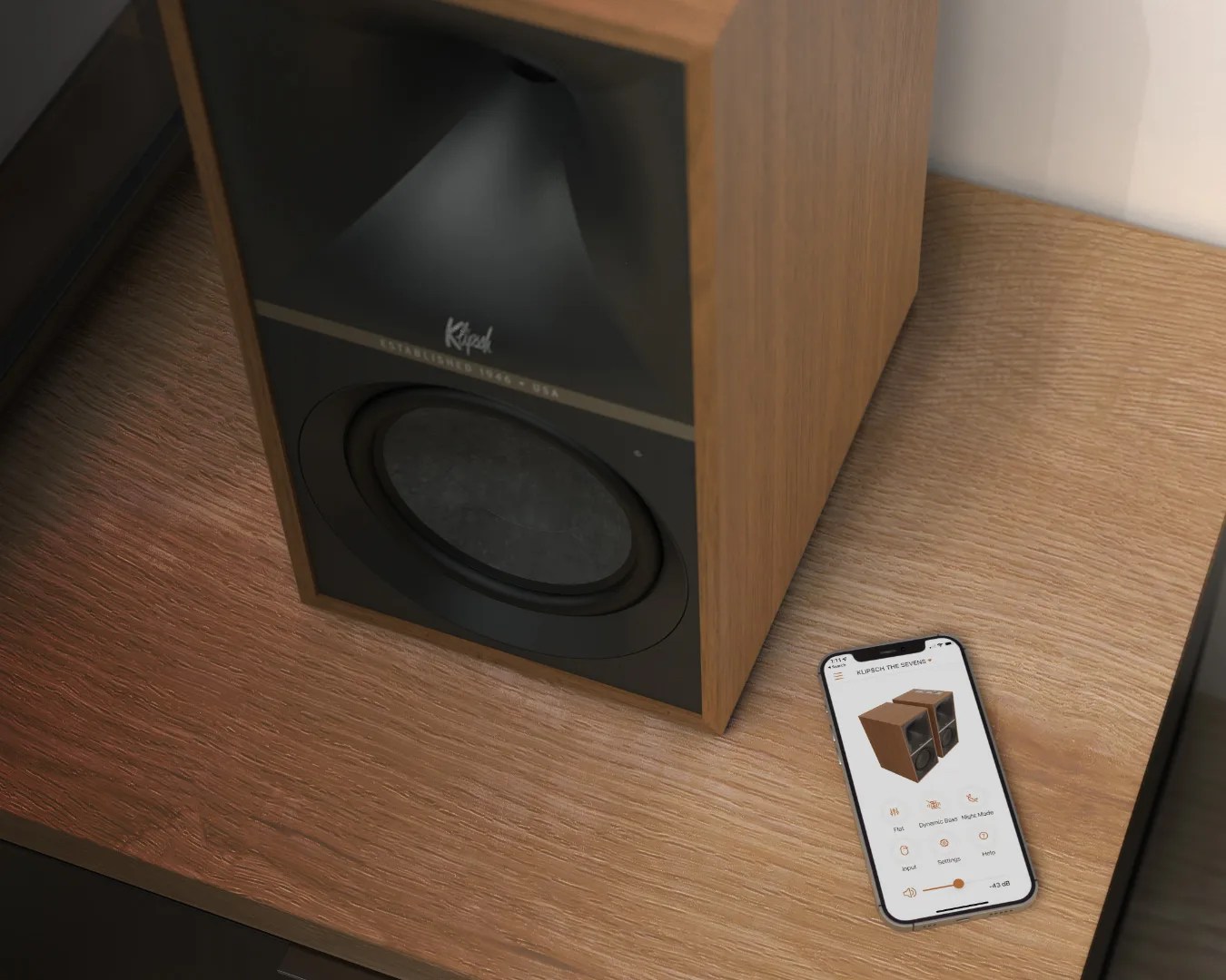 Wood-finished Klipsch speaker on a wooden surface next to a smartphone displaying speaker control app.