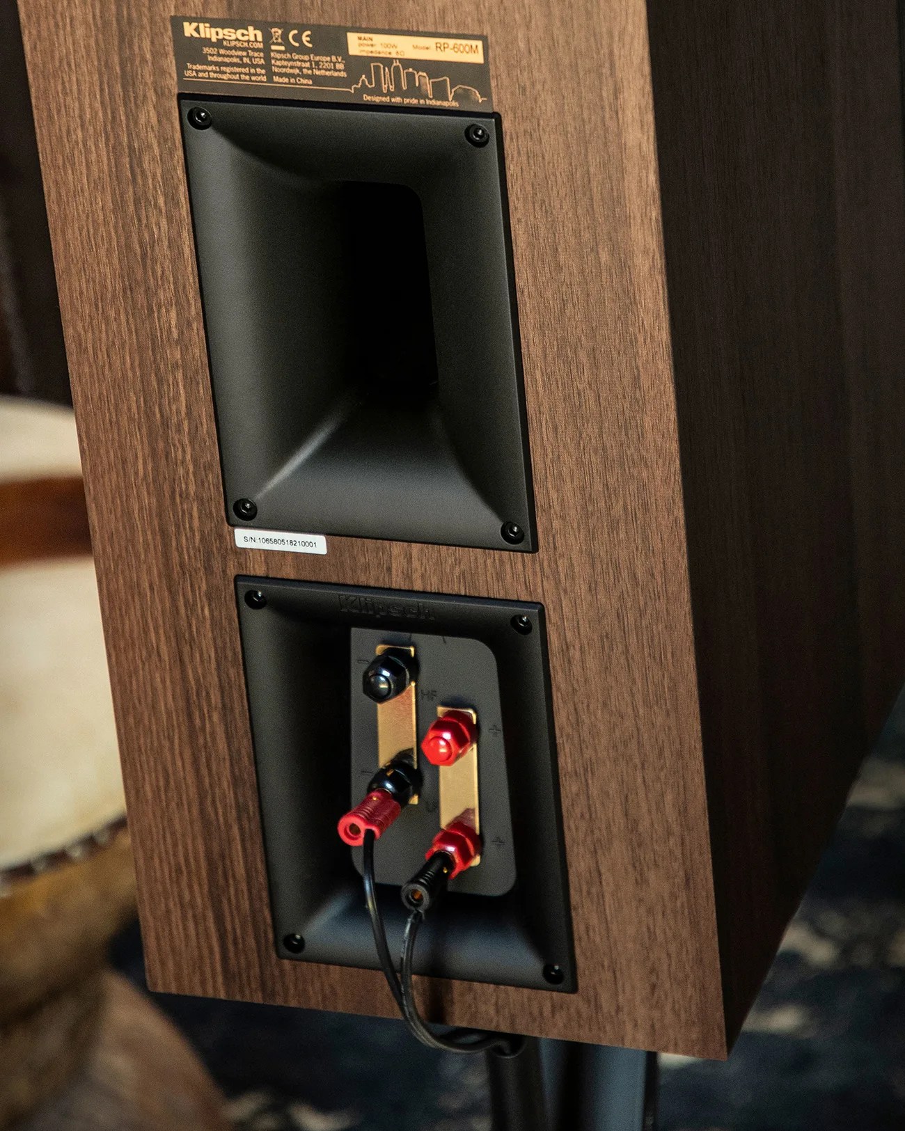 Rear view of a Klipsch RP-600M speaker with wood finish, showing input terminals with connected speaker wires.