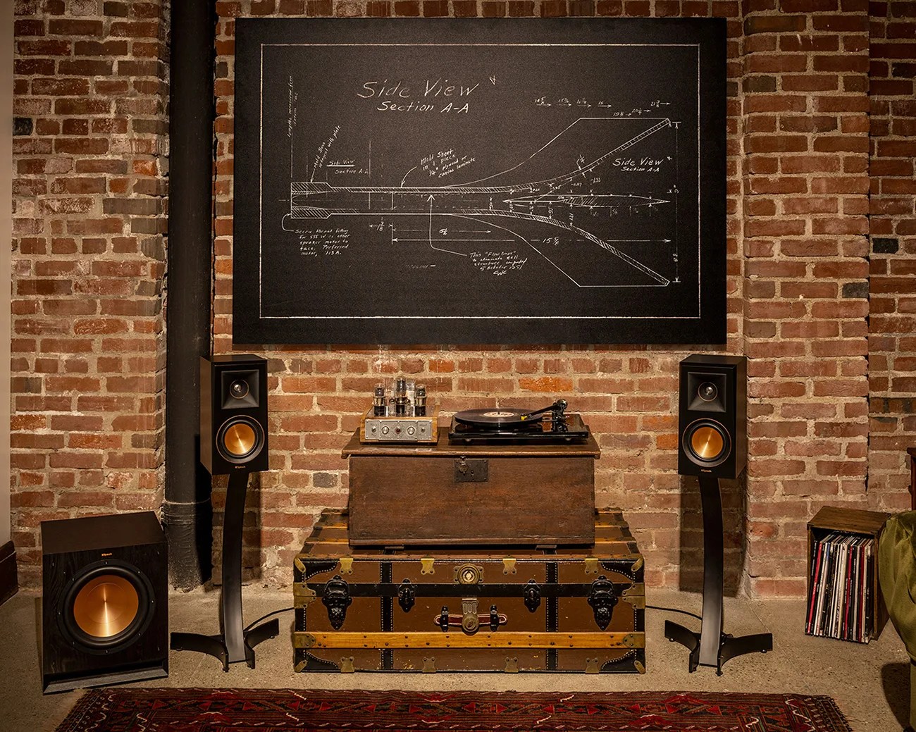 Home audio setup with black and copper speakers, vintage amplifier and turntable on a wooden chest against a brick wall.