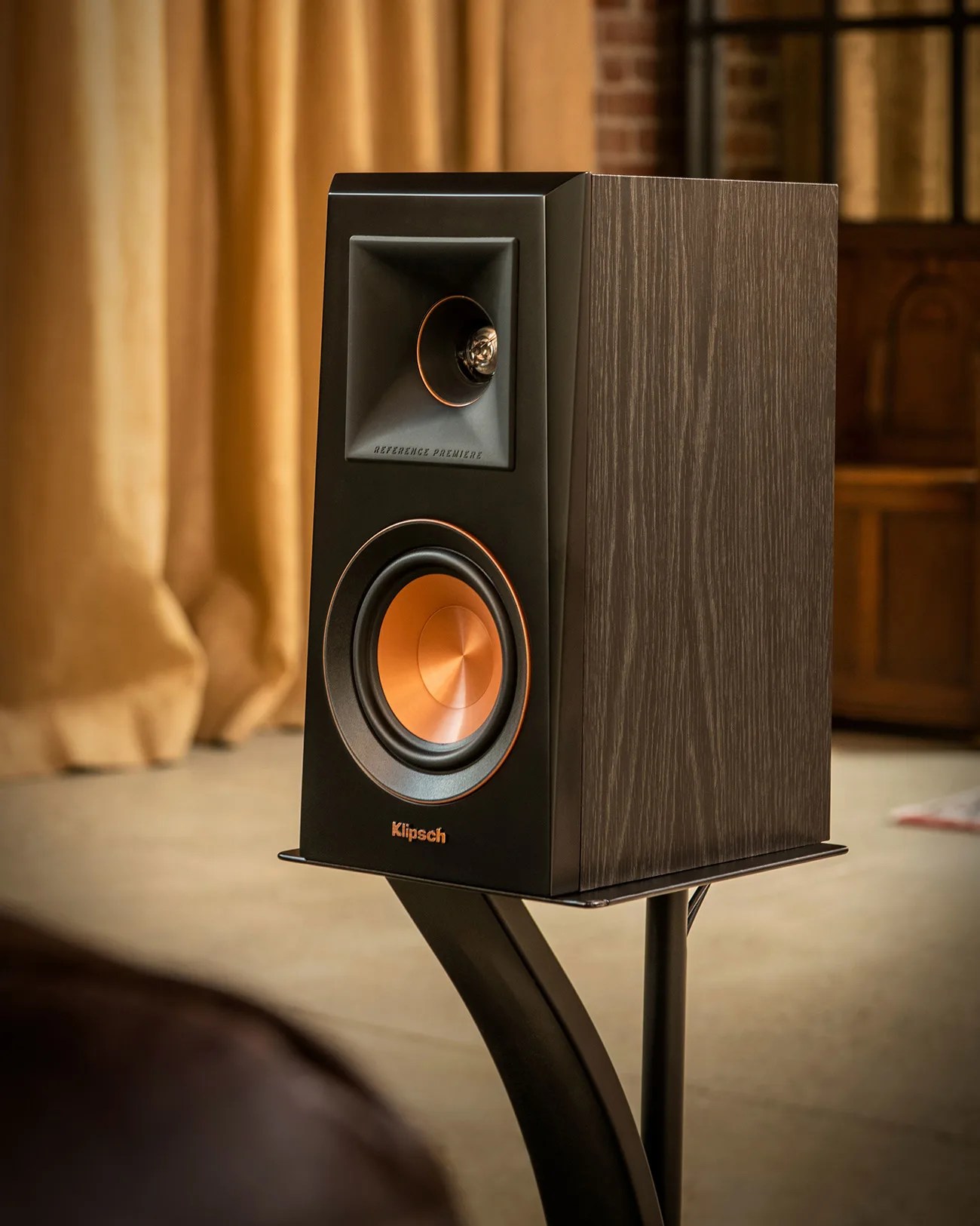 Black and wood-grain Klipsch Reference Premiere speaker with copper cone woofer on a black stand.