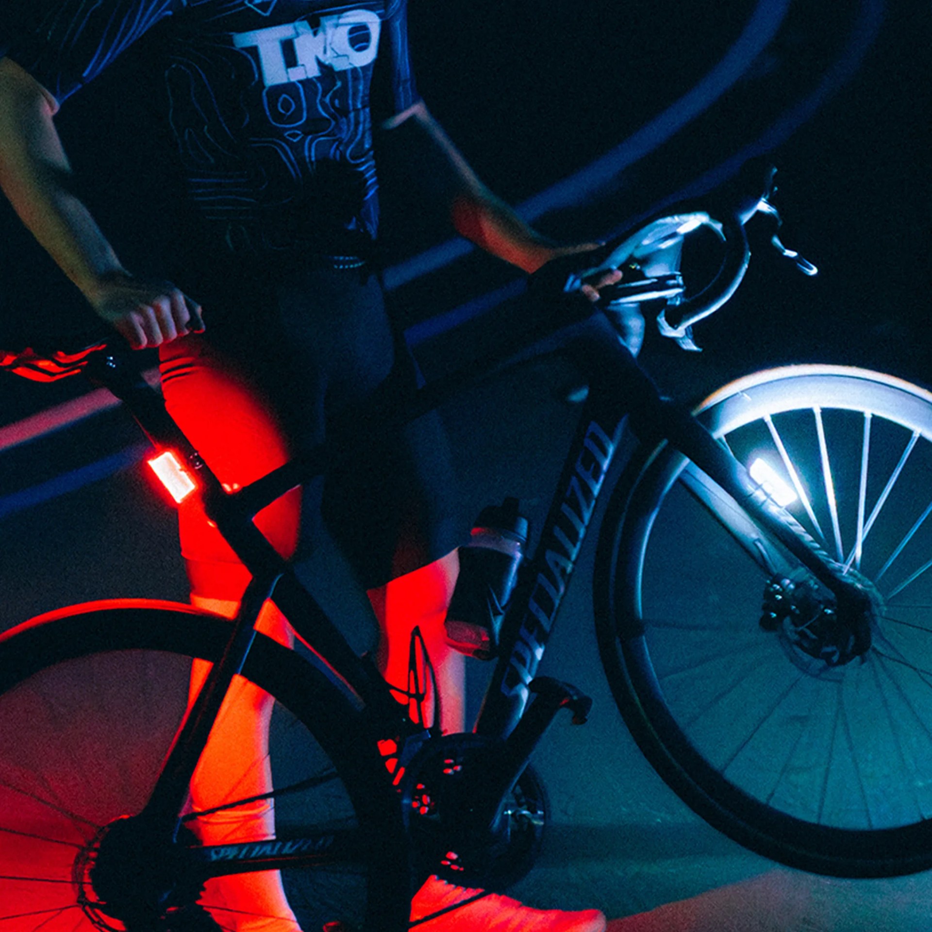 Person holding a black Specialized road bike with front white and rear red lights in low light.