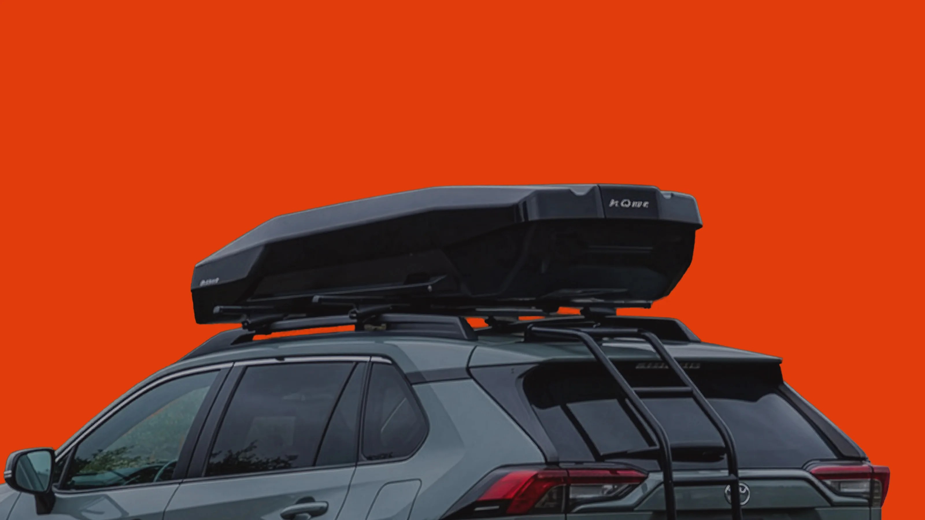 Black rooftop cargo box mounted on a gray SUV with a rear ladder against an orange background.