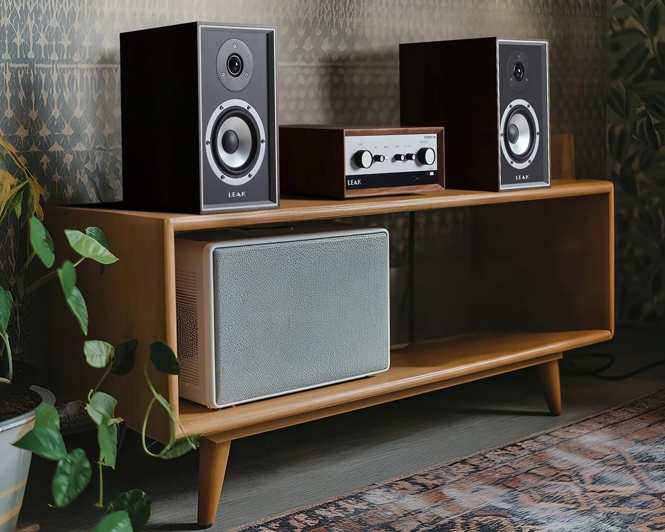 Wooden mid-century modern media console with vintage black LEAK speakers and amplifier on top, and a white speaker inside.