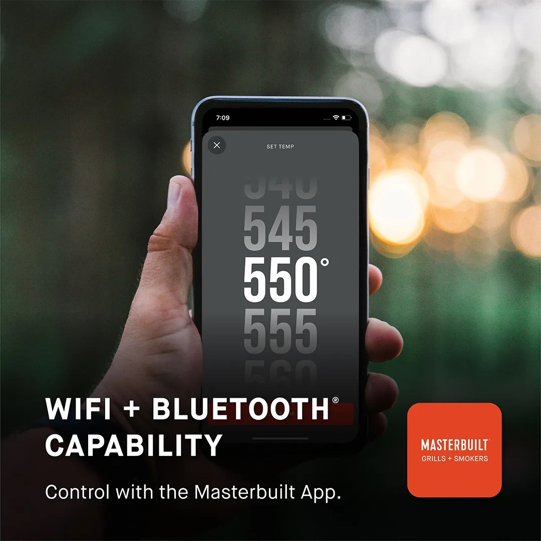 Hand holding smartphone showing temperature set to 550&deg; on Masterbuilt app with WiFi and Bluetooth capability text.