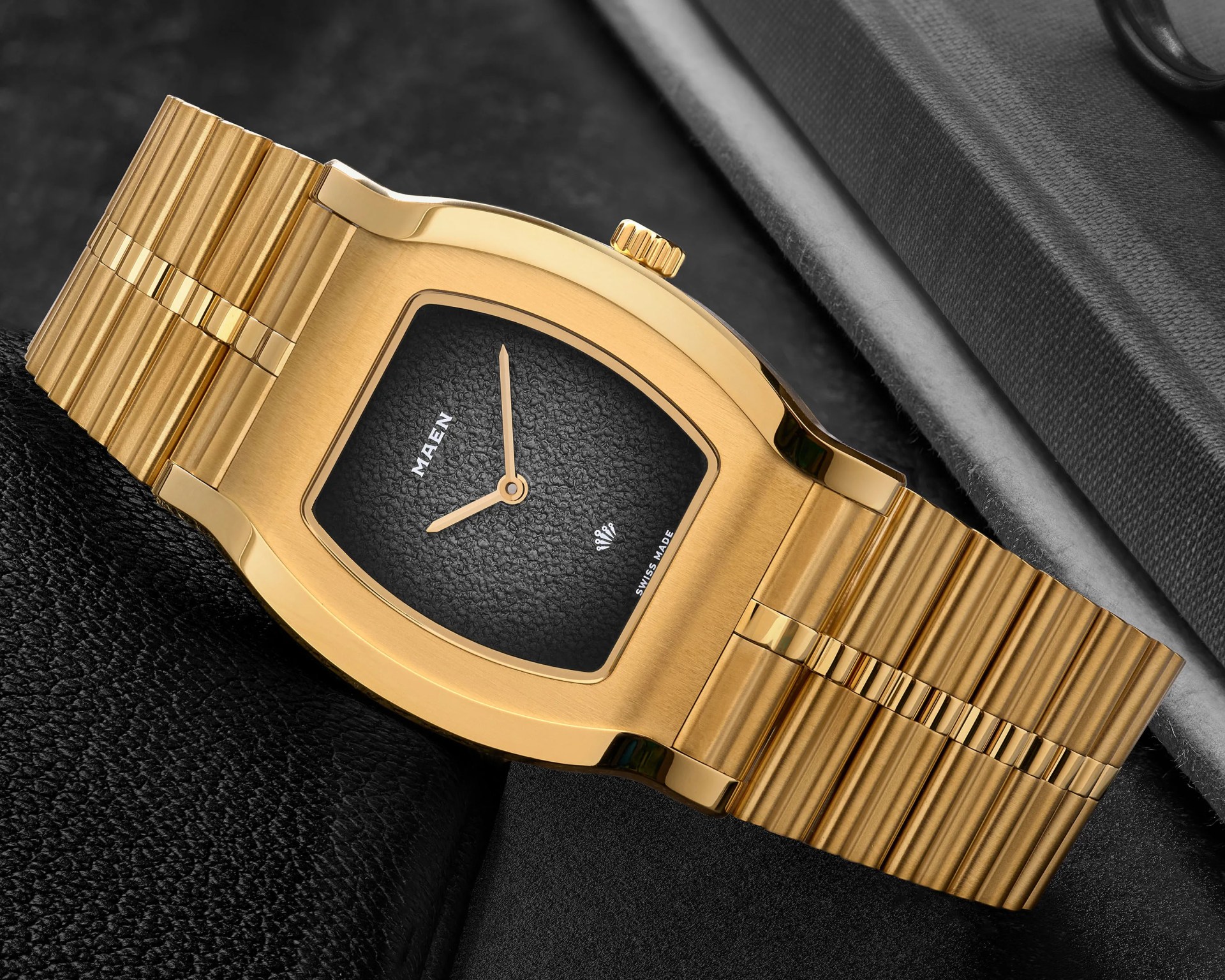 Gold-toned wristwatch with a textured black dial and integrated ribbed metal bracelet.
