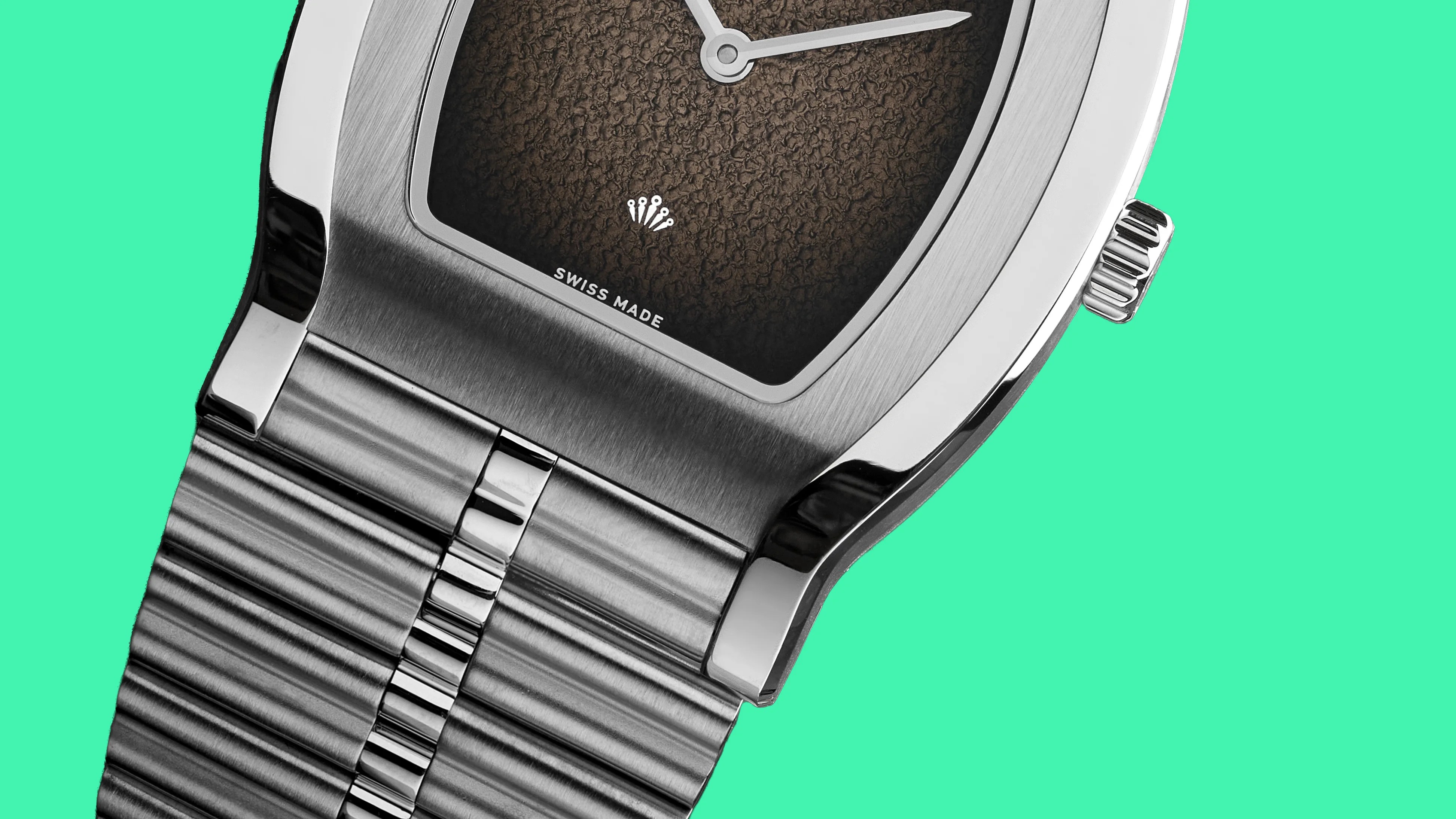 Close-up of a stainless steel wristwatch with a textured brown dial and a brushed metal bracelet against a green background.