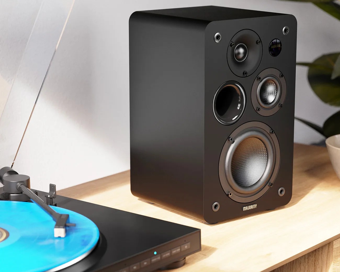 Black Majority bookshelf speaker with multiple drivers on a wooden surface next to a turntable with a blue vinyl record.