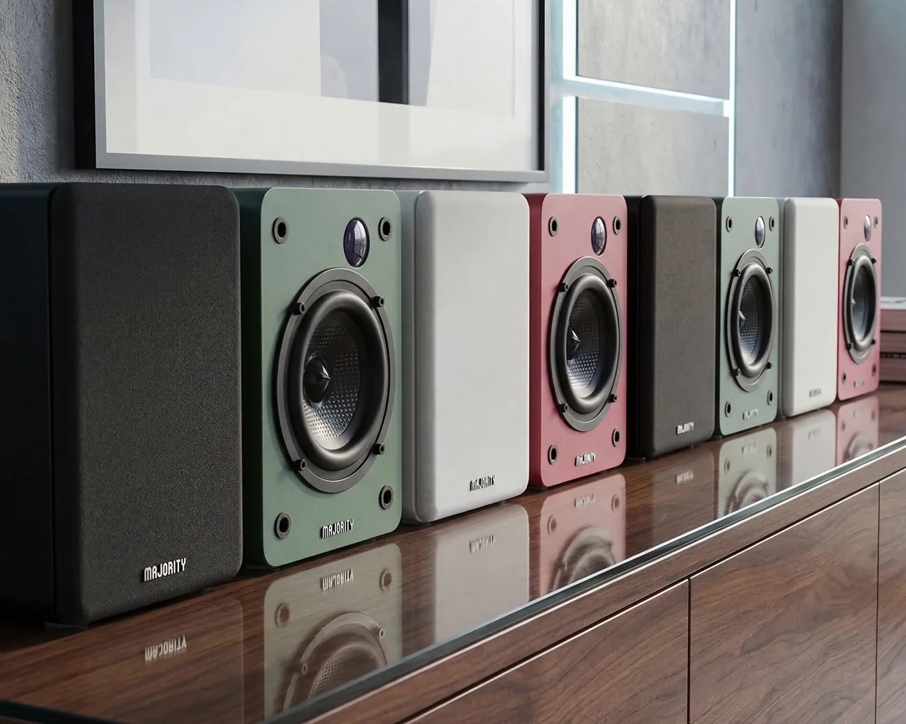 Six rectangular bookshelf speakers in black, green, white, and pink colors lined up on a wooden surface.
