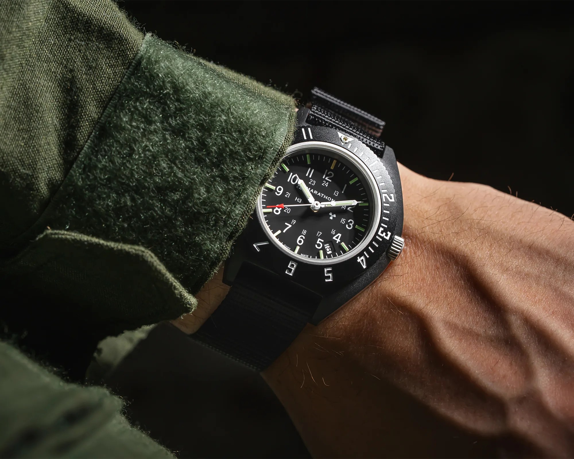 Black Marathon wristwatch with white numerals and green accents on a black fabric strap worn on a wrist.