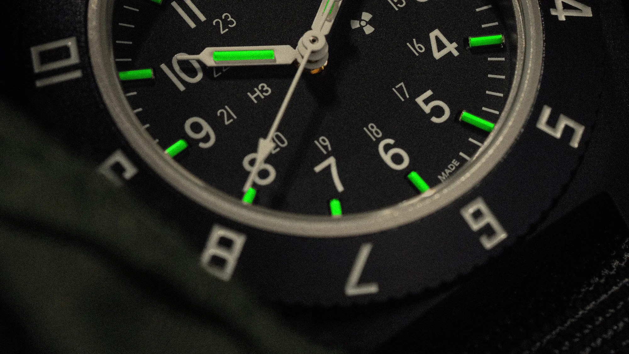 Close-up of a black watch face with white numbers and green luminescent markers on the hands and hour indices.