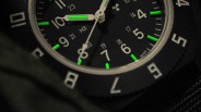 Close-up of a black watch face with white numbers and green luminescent markers on the hands and hour indices.
