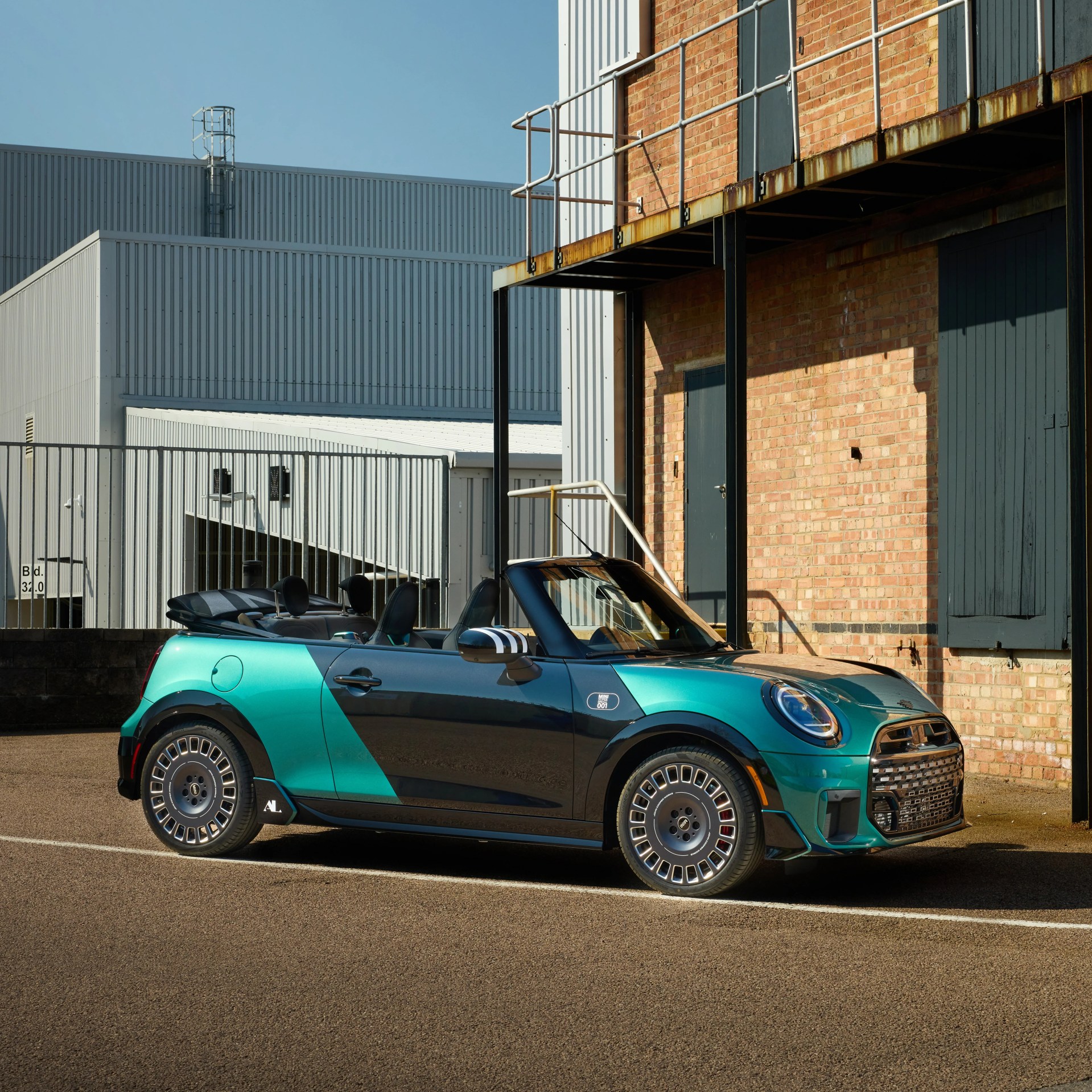 Convertible Mini Cooper with teal and black geometric paint parked beside a brick building.